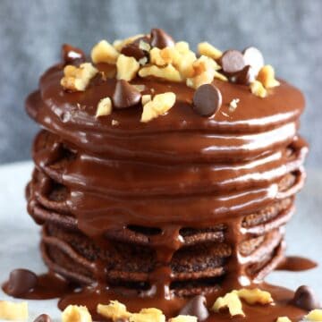 A stack of gluten-free vegan chocolate pancakes covered with chocolate sauce, chopped walnuts and chocolate chips