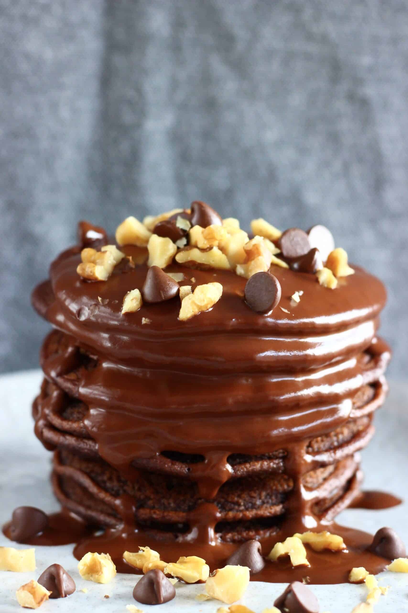 A stack of gluten-free vegan chocolate pancakes covered with chocolate sauce, chopped walnuts and chocolate chips