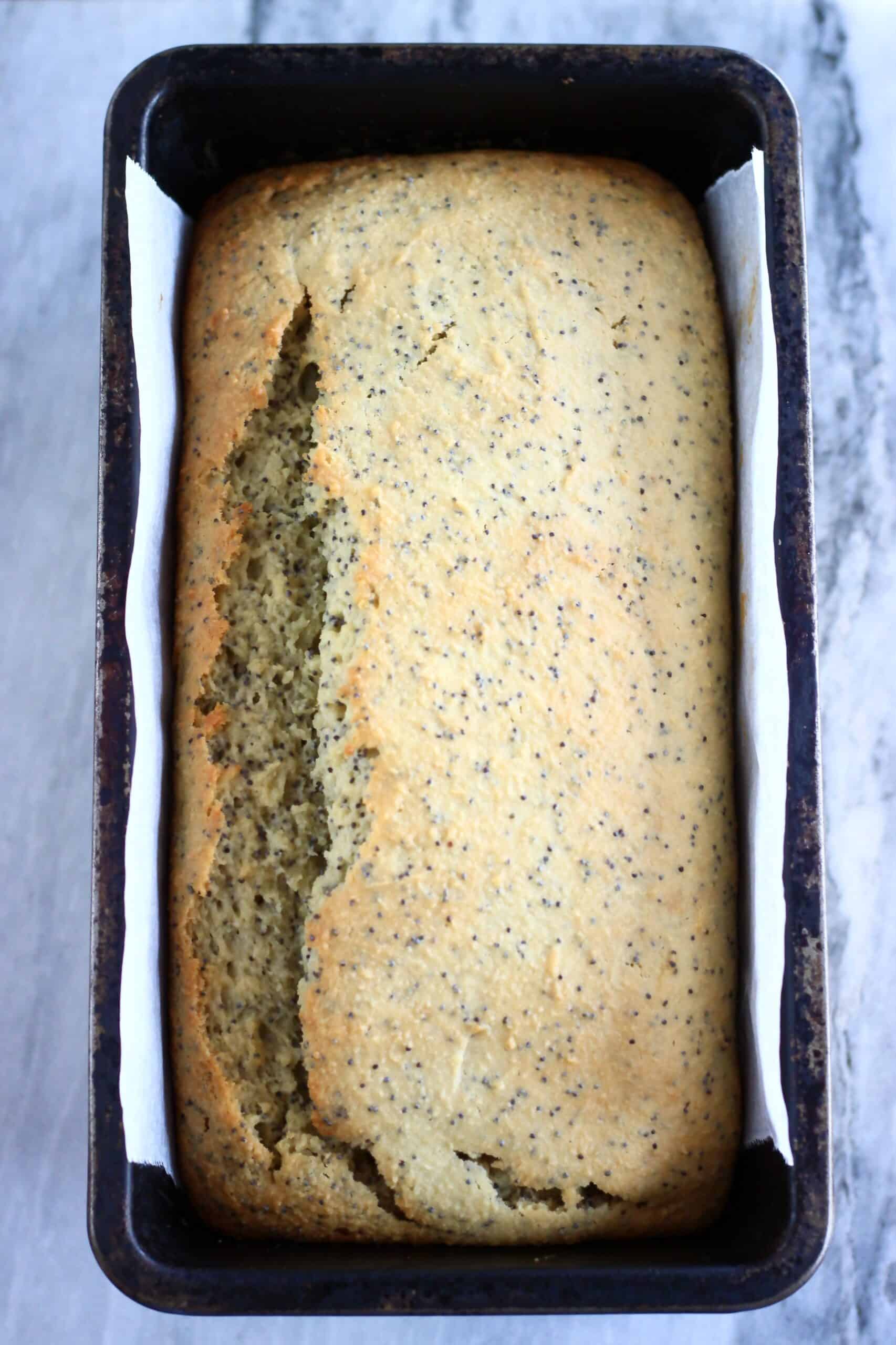 A loaf of baked gluten-free vegan orange poppy seed bread in a loaf tin lined with baking paper