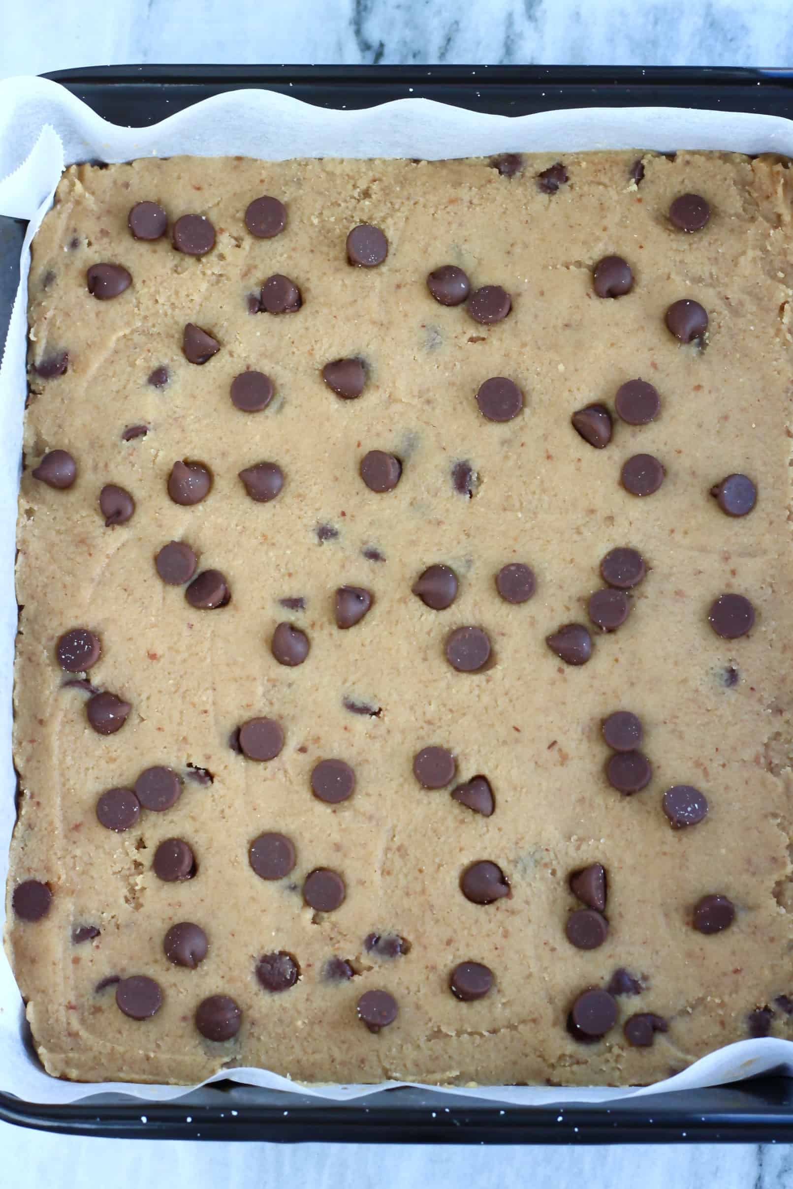 Raw vegan gluten-free blondies batter with chocolate chips in a baking tin lined with baking paper
