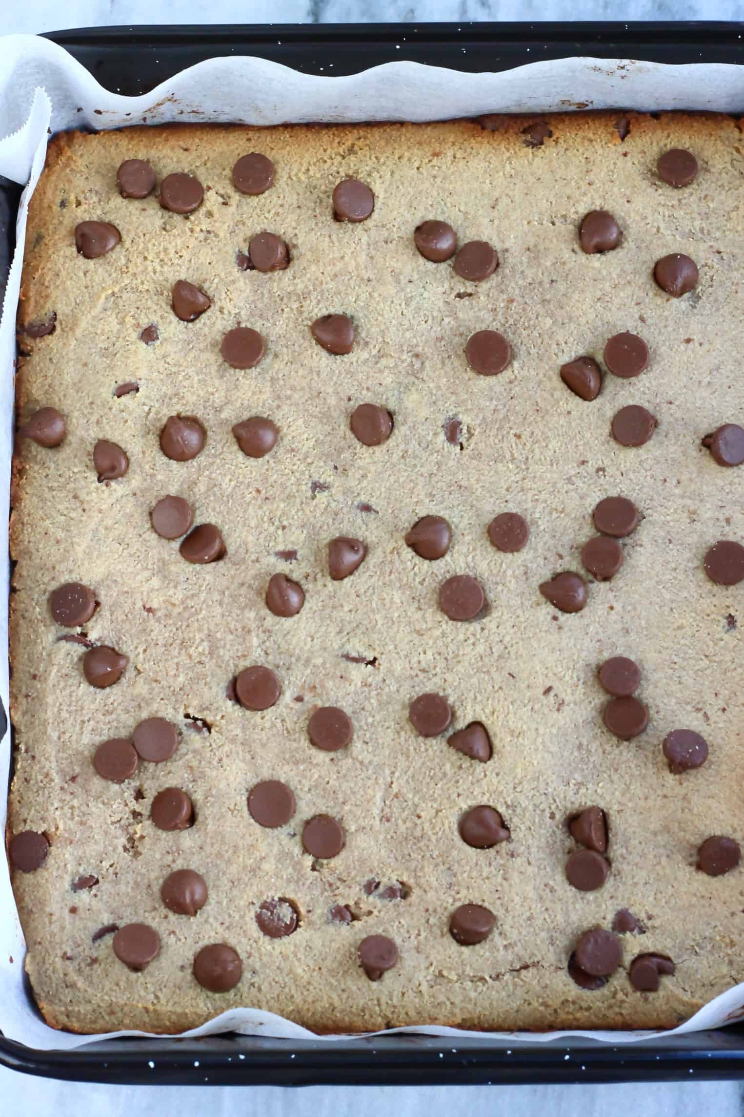 Baked vegan gluten-free blondies with chocolate chips in a baking tin lined with baking paper