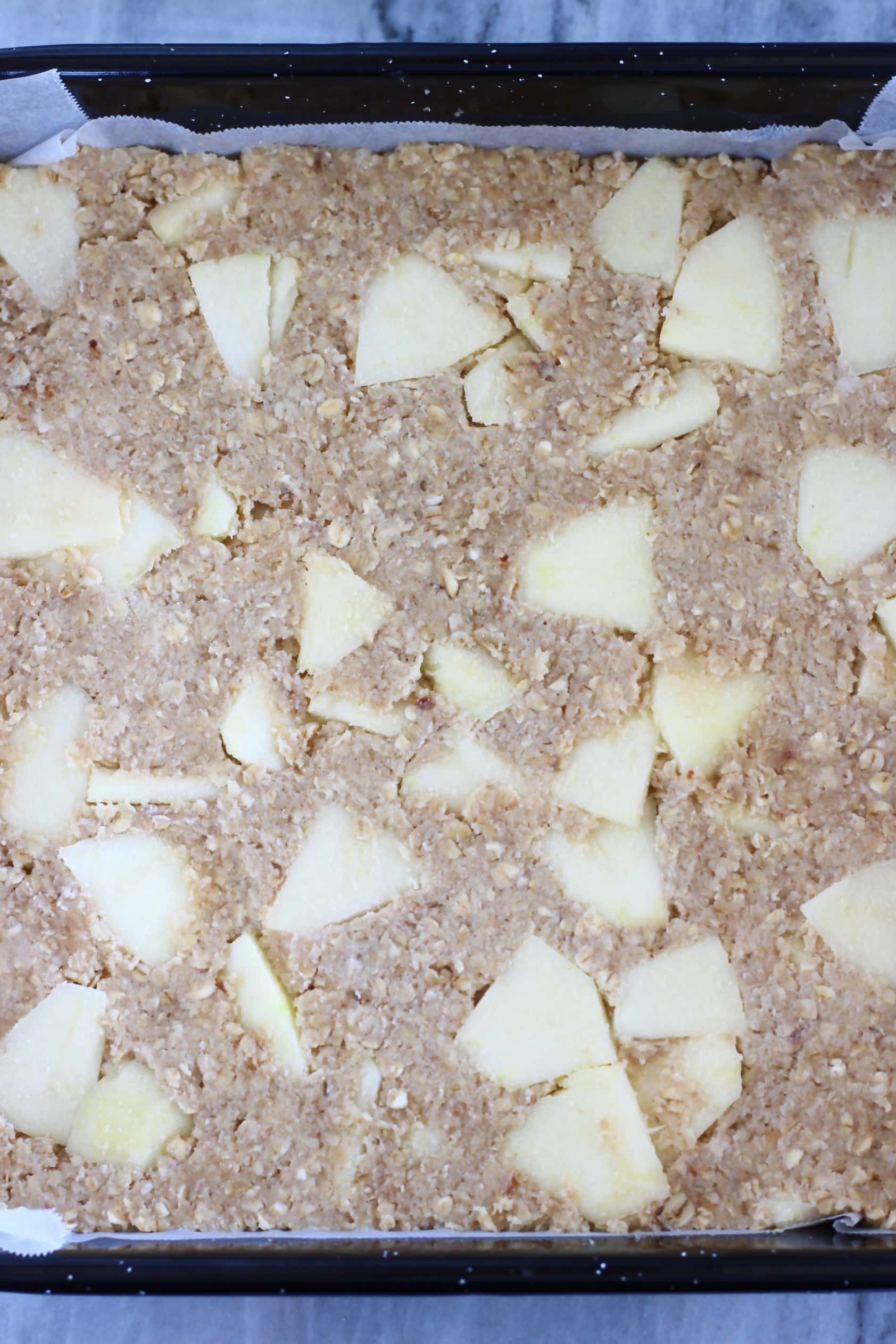 Raw vegan apple oatmeal bars mixture in a square baking tin lined with baking paper