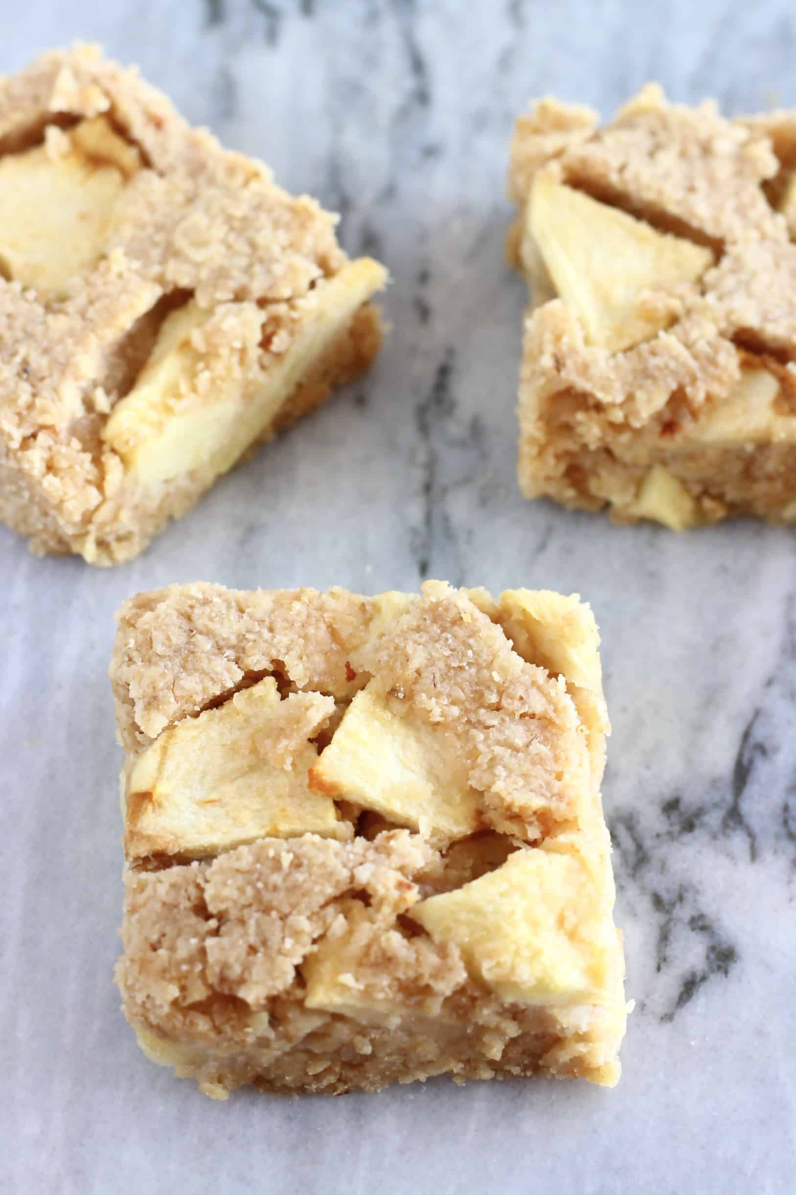 Three square pieces of vegan apple oatmeal bars on a marble background
