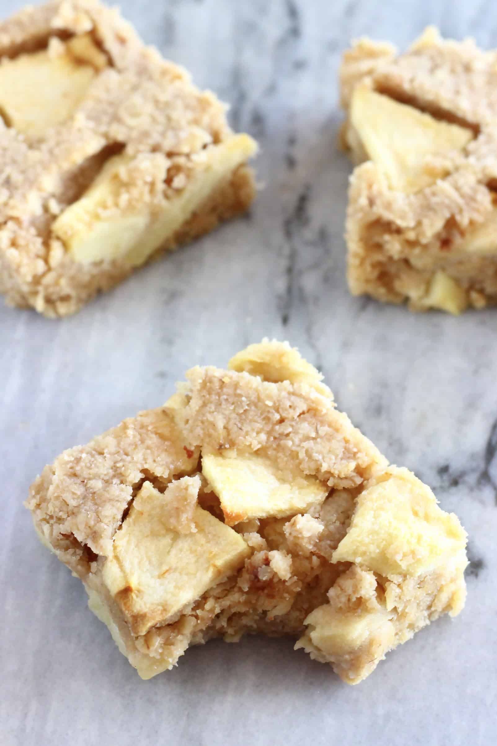 Three vegan apple oatmeal bars with a bite taken out of one on a marble background