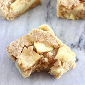 Three vegan apple oatmeal bars with a bite taken out of one on a marble background