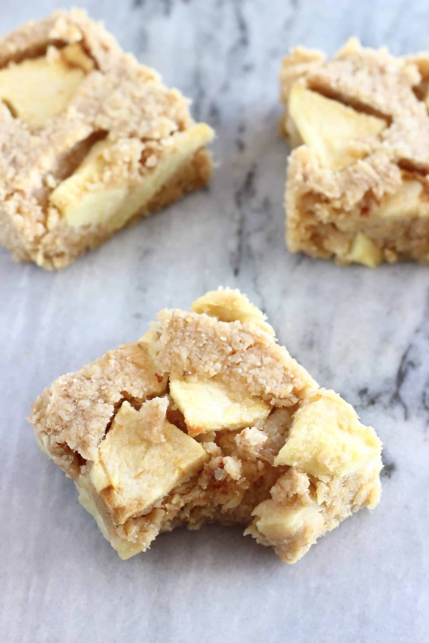 Three vegan apple oatmeal bars with a bite taken out of one on a marble background