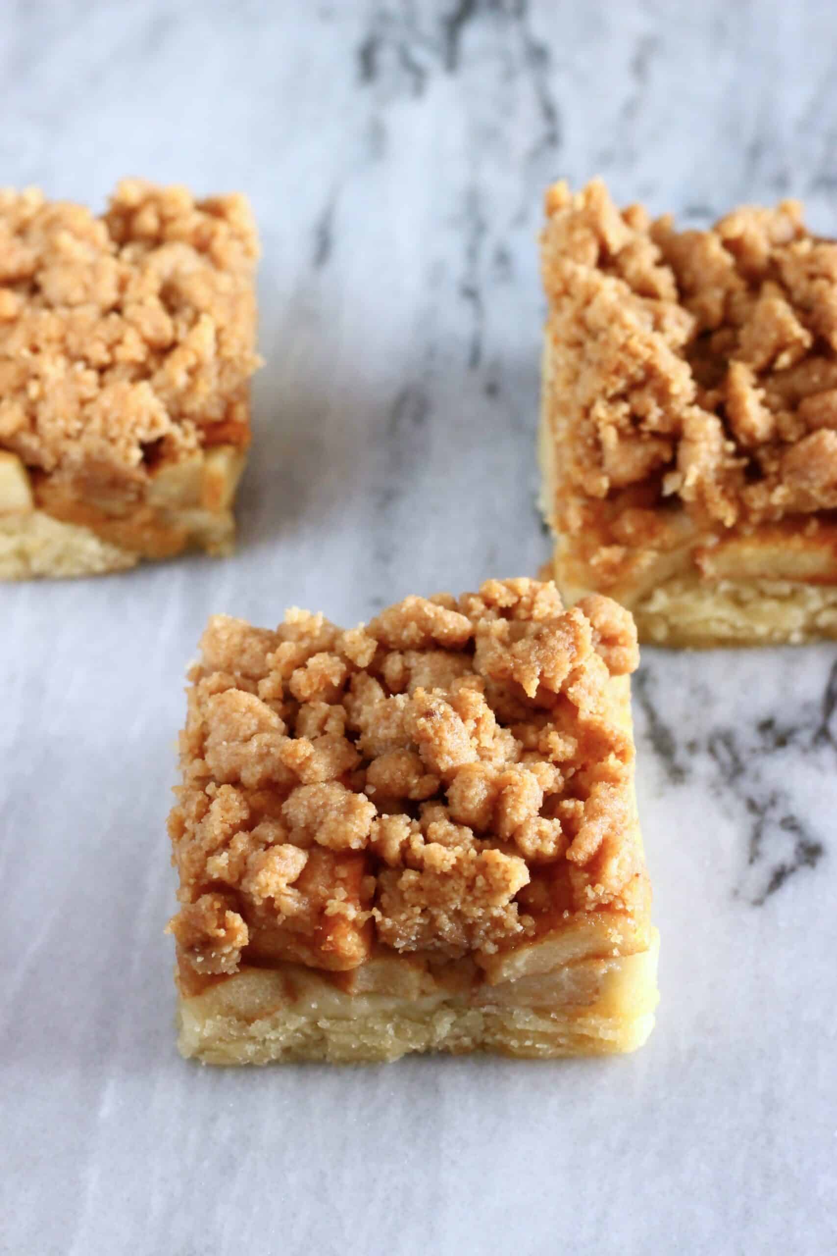Three square pieces of vegan apple crumb cake on a marble background