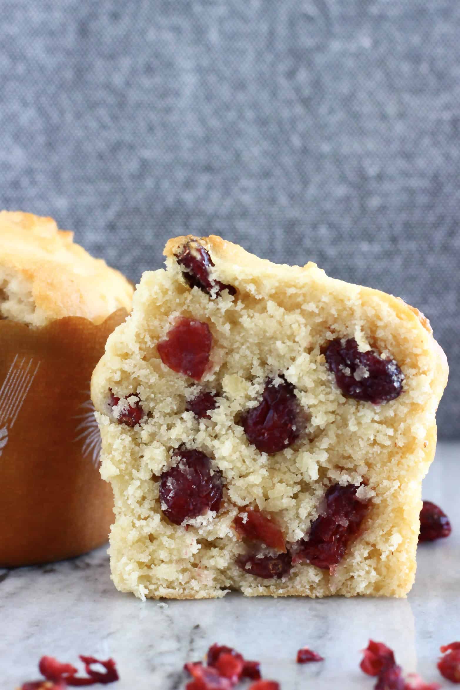 A halved gluten-free vegan cranberry muffin on a marble background