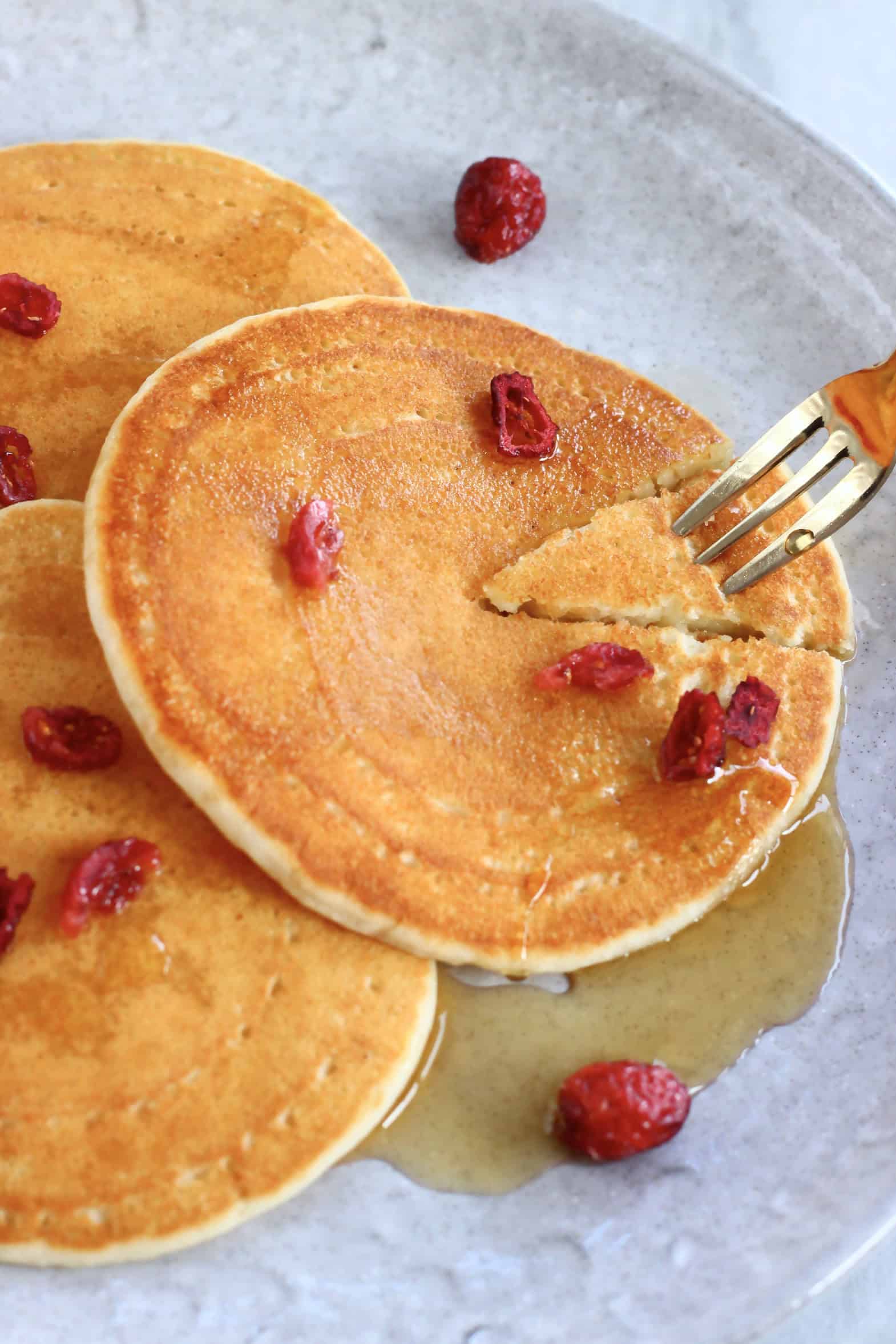 Three vegan buttermilk pancakes with maple syrup on a plate and a gold fork