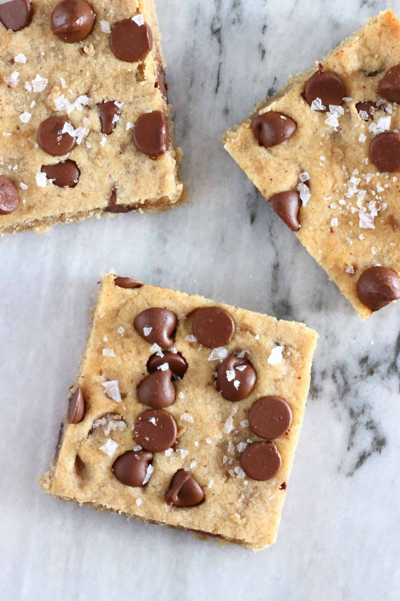 Three gluten-free vegan chocolate chip cookie bars with sea salt on a marble background
