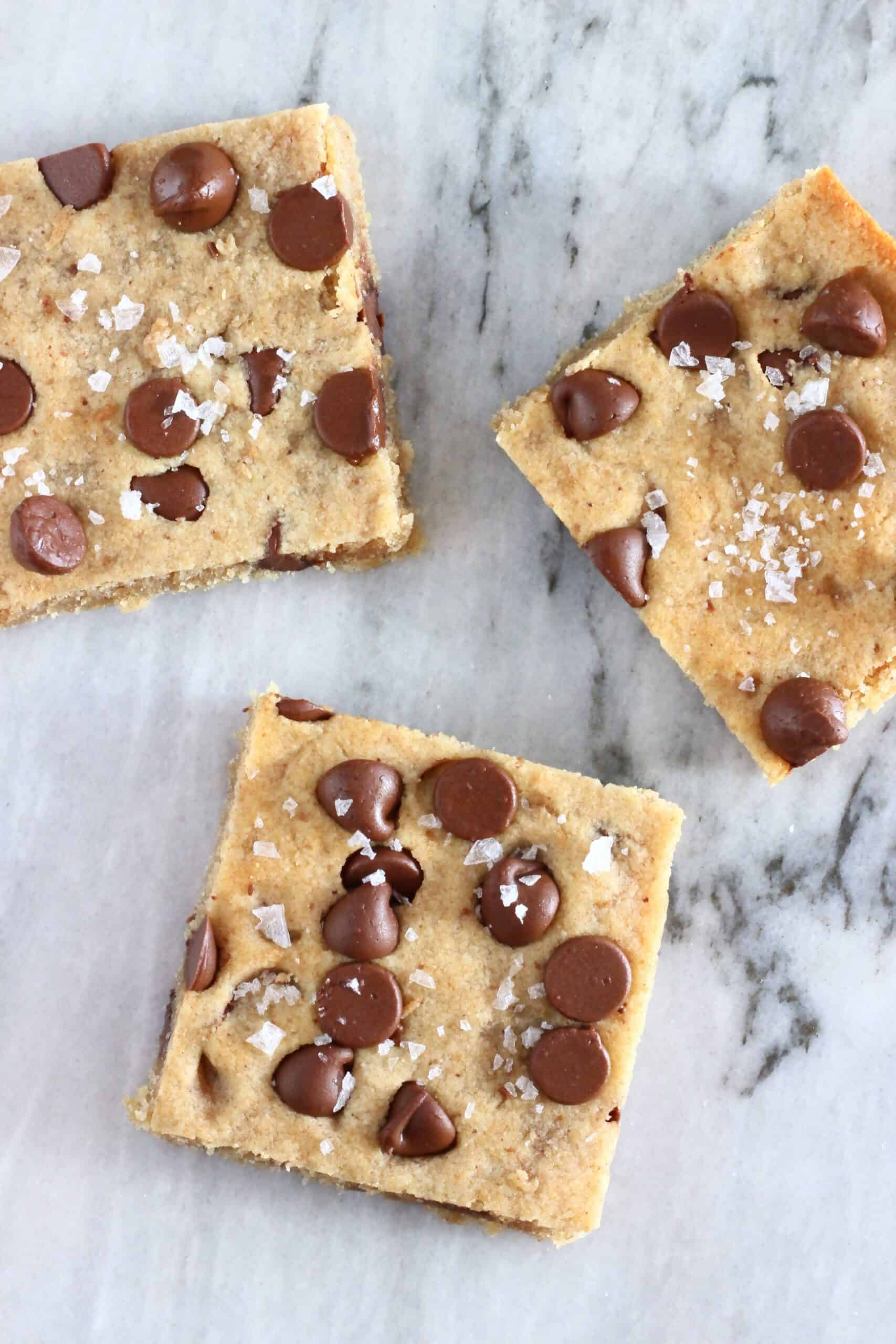 Three gluten-free vegan chocolate chip cookie bars with sea salt on a marble background
