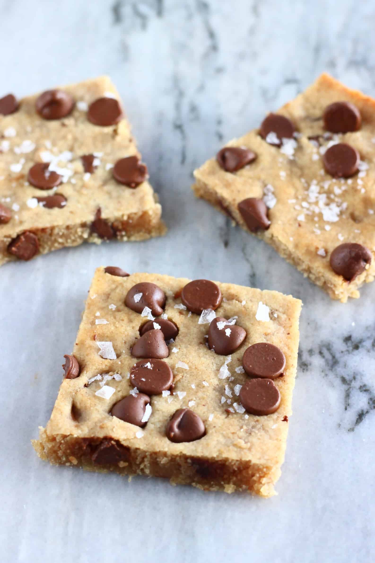Three gluten-free vegan chocolate chip cookie bars with sea salt on a marble background