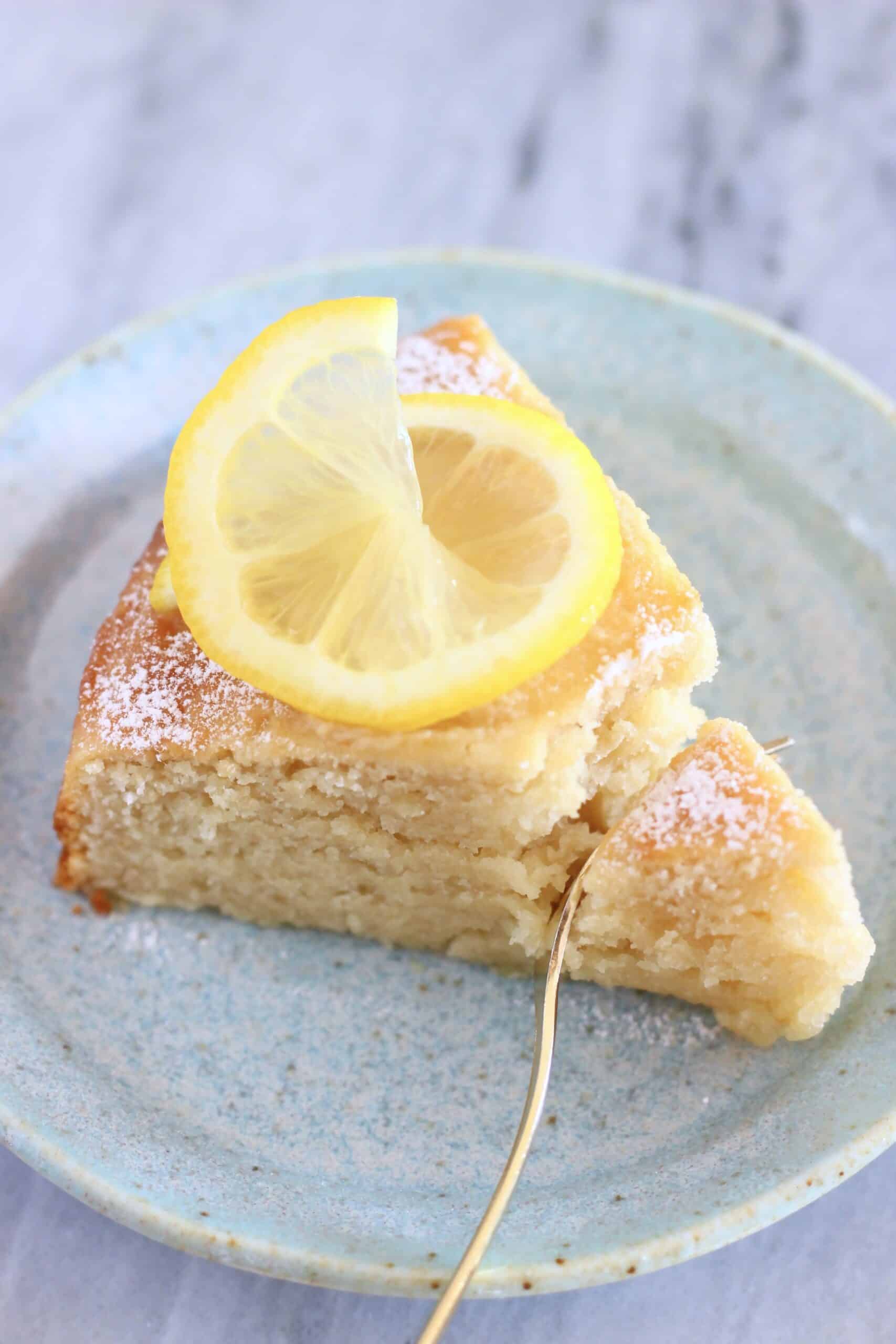 A slice of gluten-free vegan lemon yogurt cake on a plate with a fork taking a bite out of it