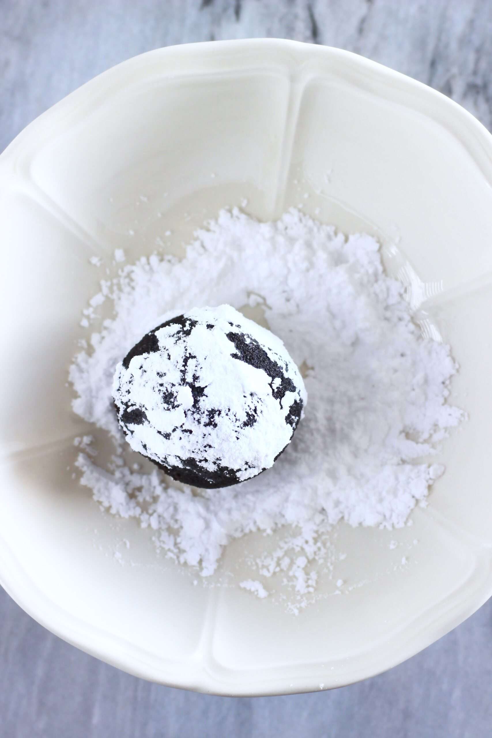 A ball of gluten-free vegan chocolate cookie dough in a bowl of powdered sugar
