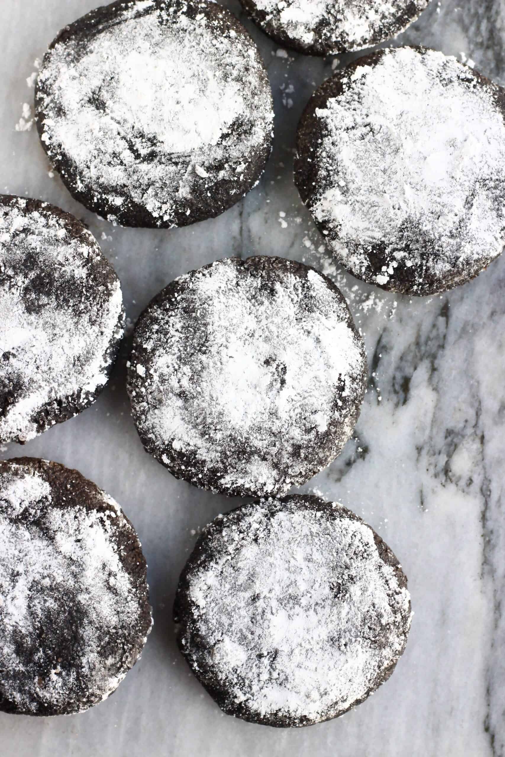 Six gluten-free vegan chocolate crinkle cookies on a marble background