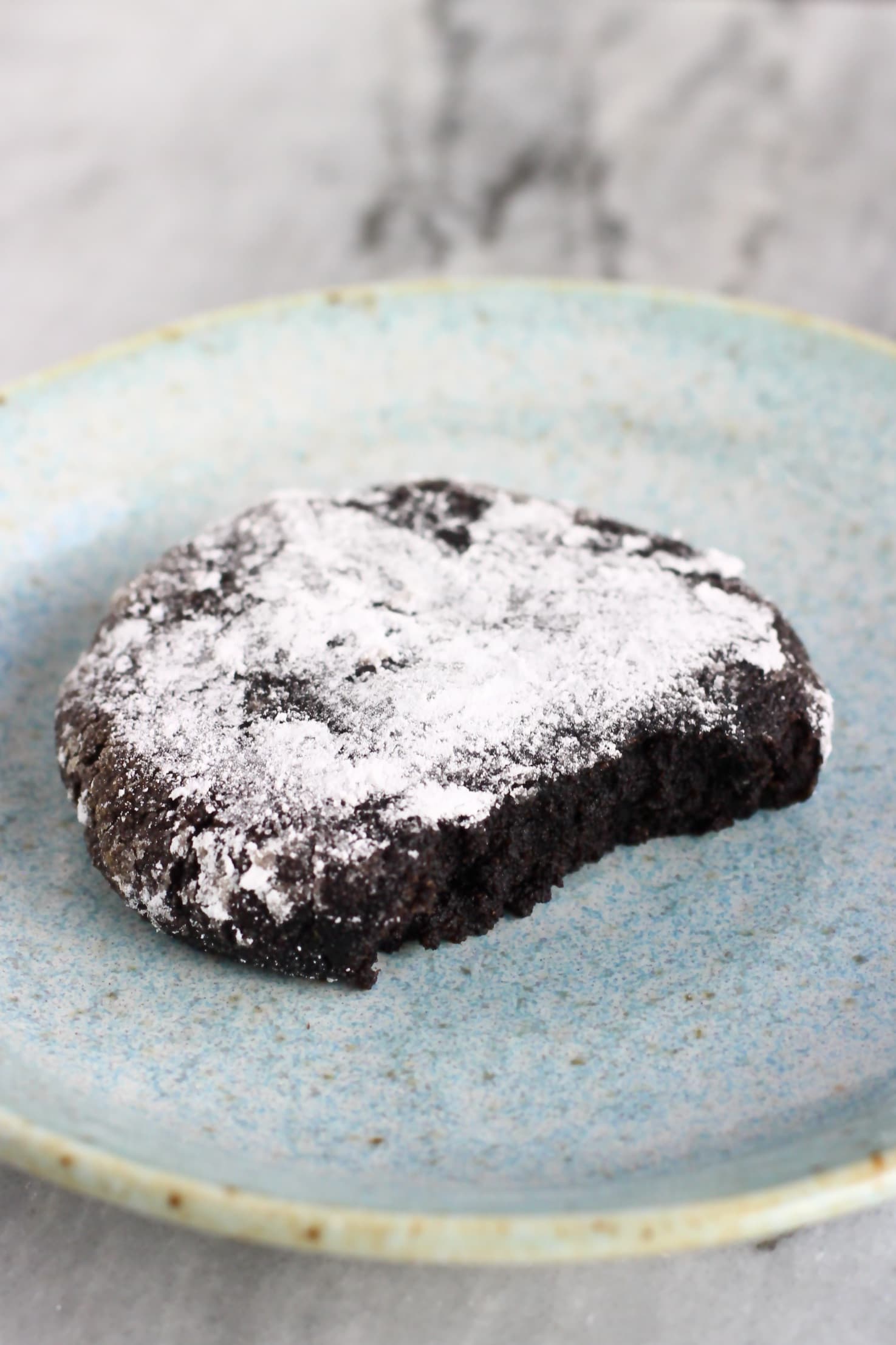 A gluten-free vegan chocolate crinkle cookie on a plate with a bite taken out of it