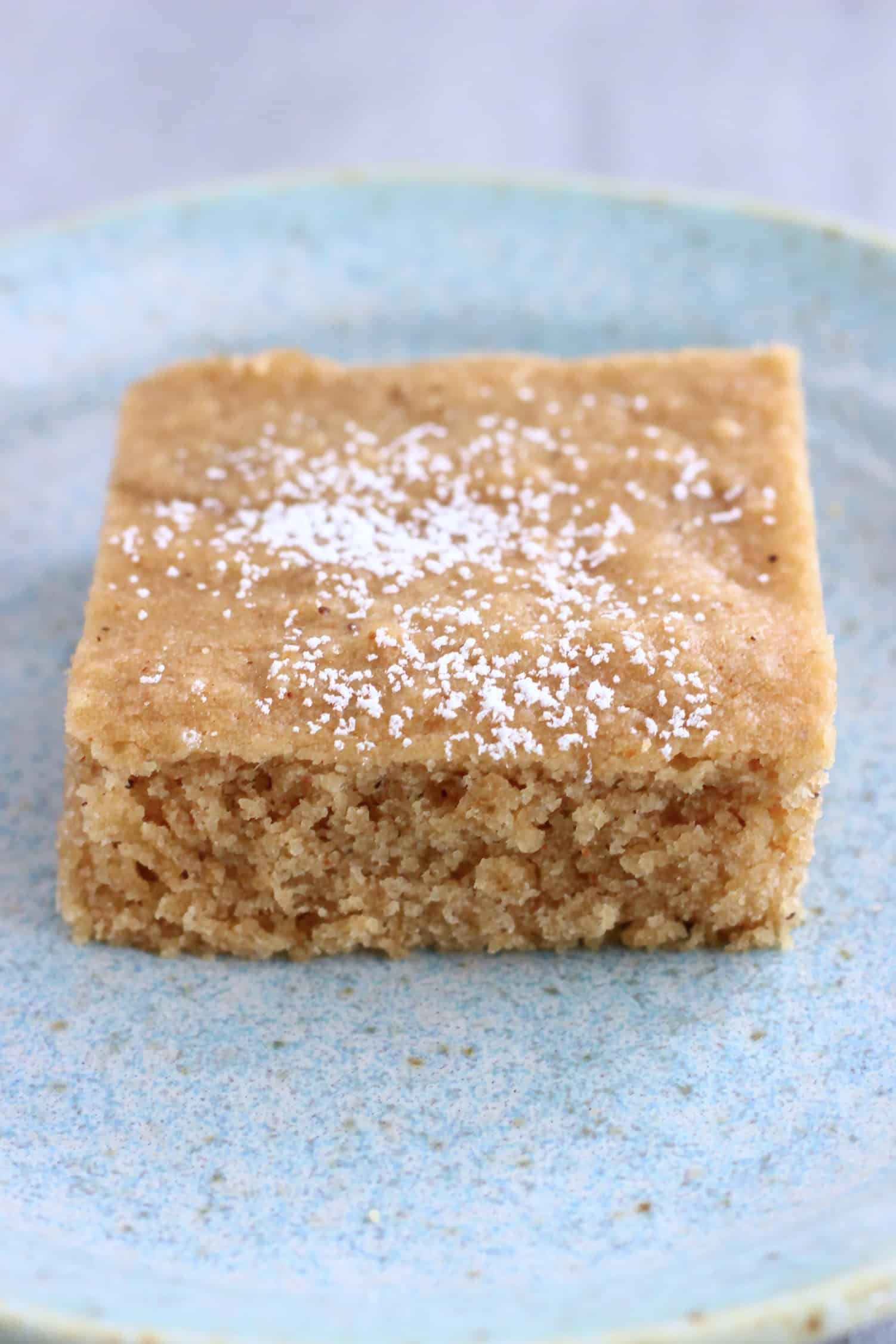 A square slice of gluten-free vegan gingerbread snack cake topped with powdered sugar on a plate