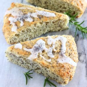 Three triangular gluten-free vegan lemon poppy seed scones on a marble background