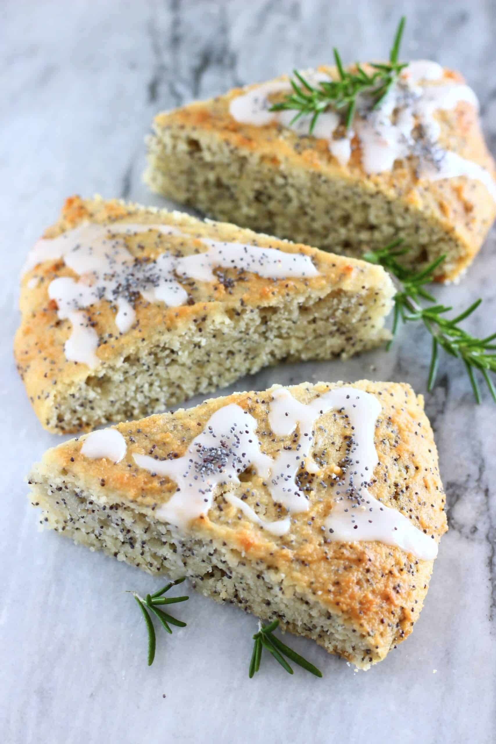 Three triangular gluten-free vegan lemon poppy seed scones on a marble background