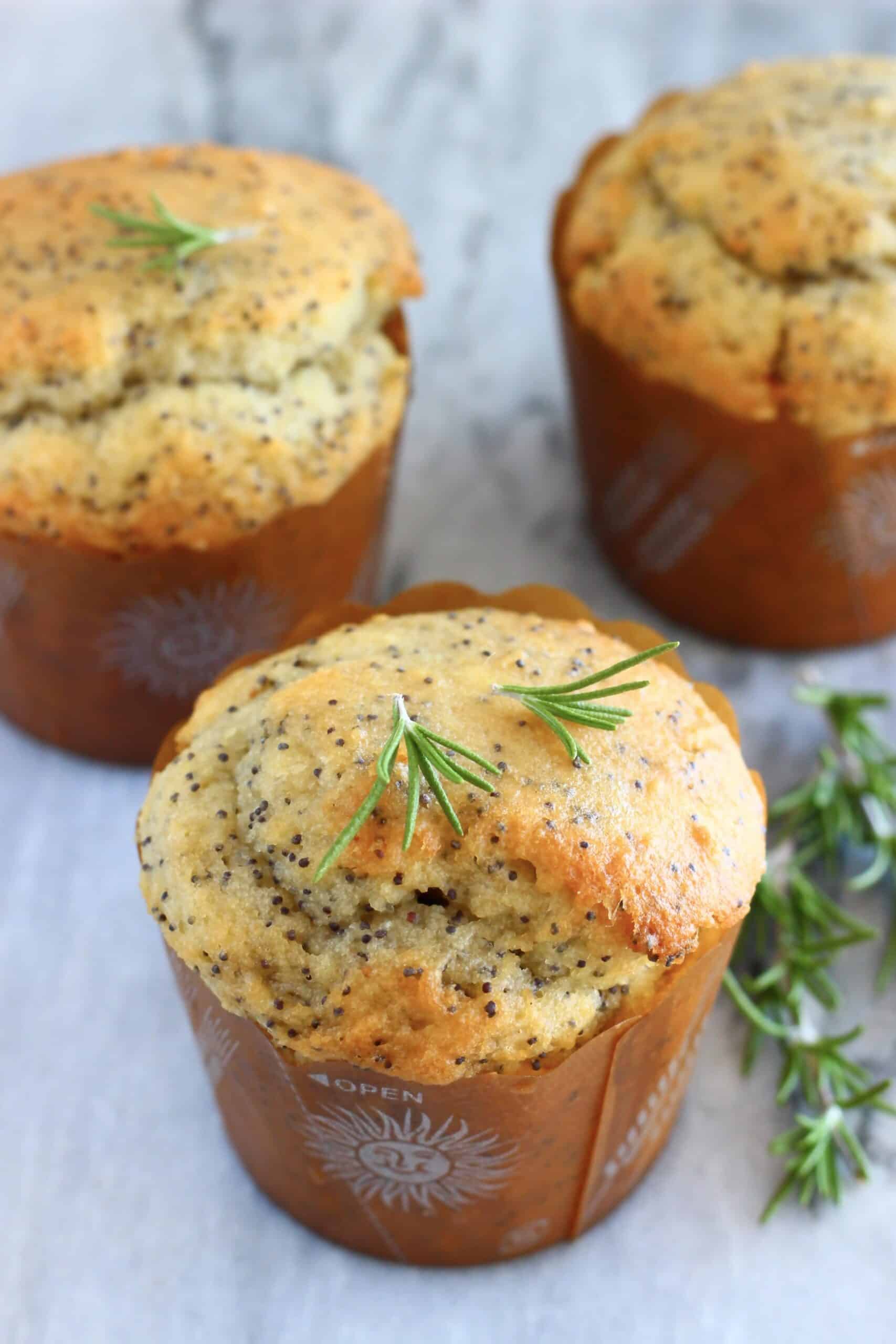 Three gluten-free vegan orange poppy seed muffins on a marble background