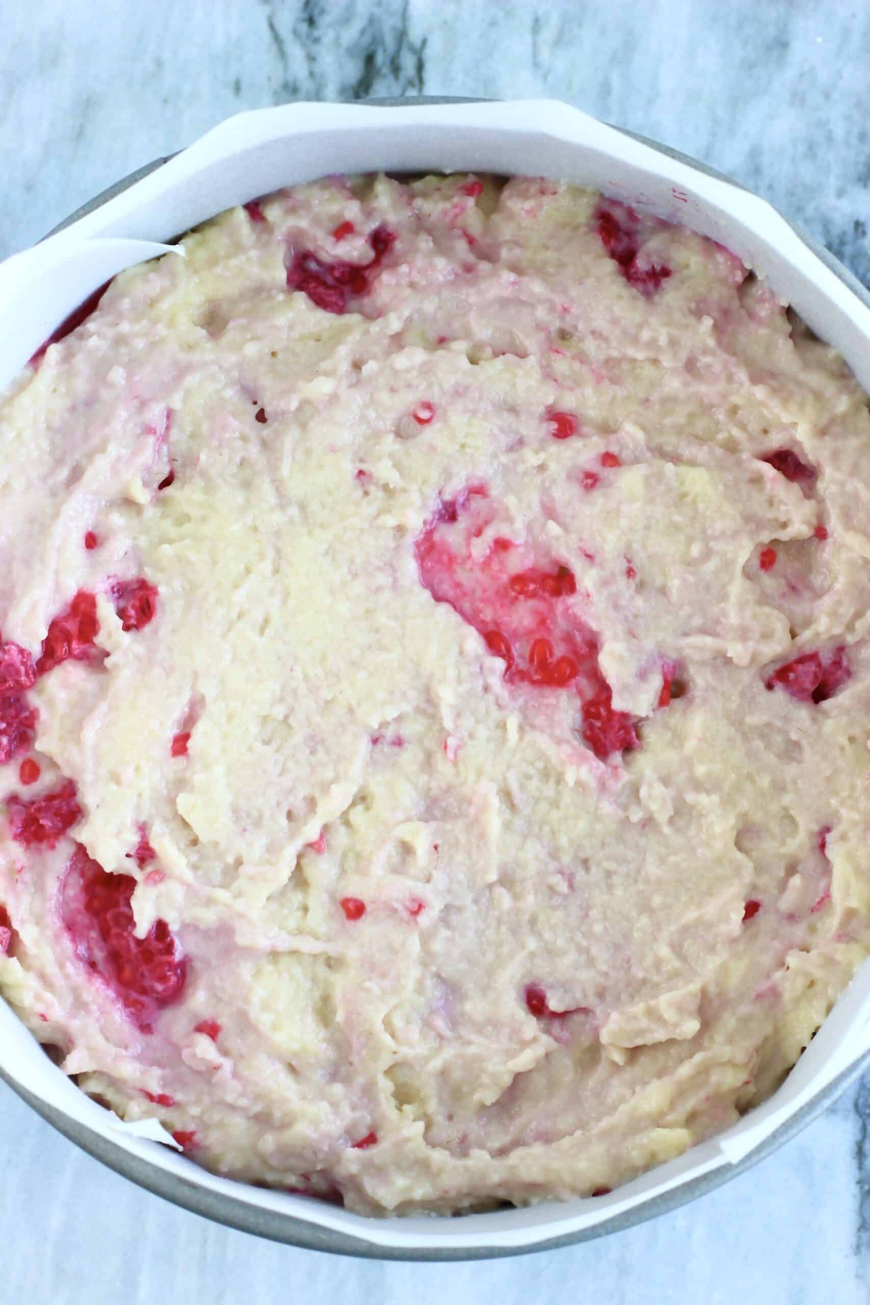 Raw gluten-free vegan raspberry cake batter in a round springform baking tin lined with baking paper