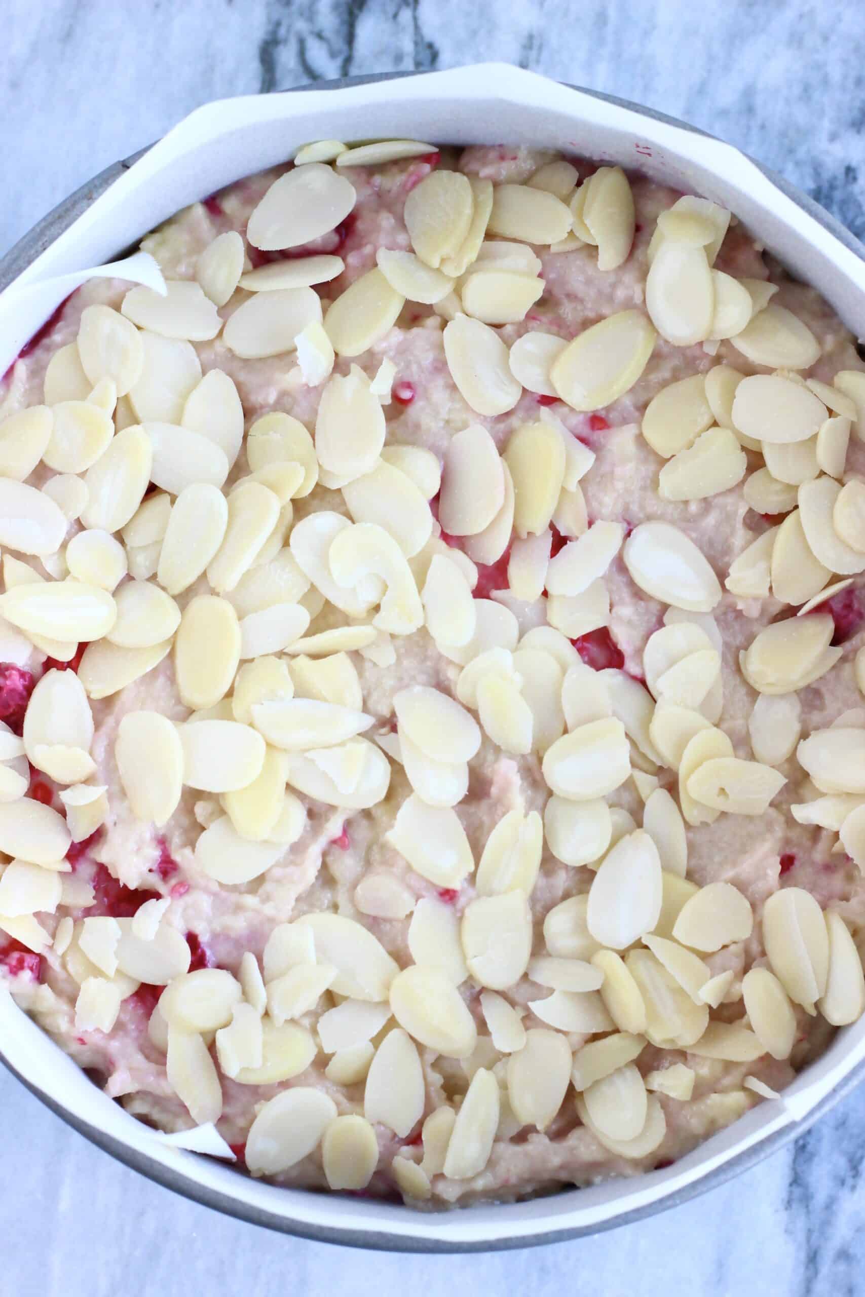 Raw gluten-free vegan raspberry cake batter topped with flaked almonds in a round springform baking tin lined with baking paper