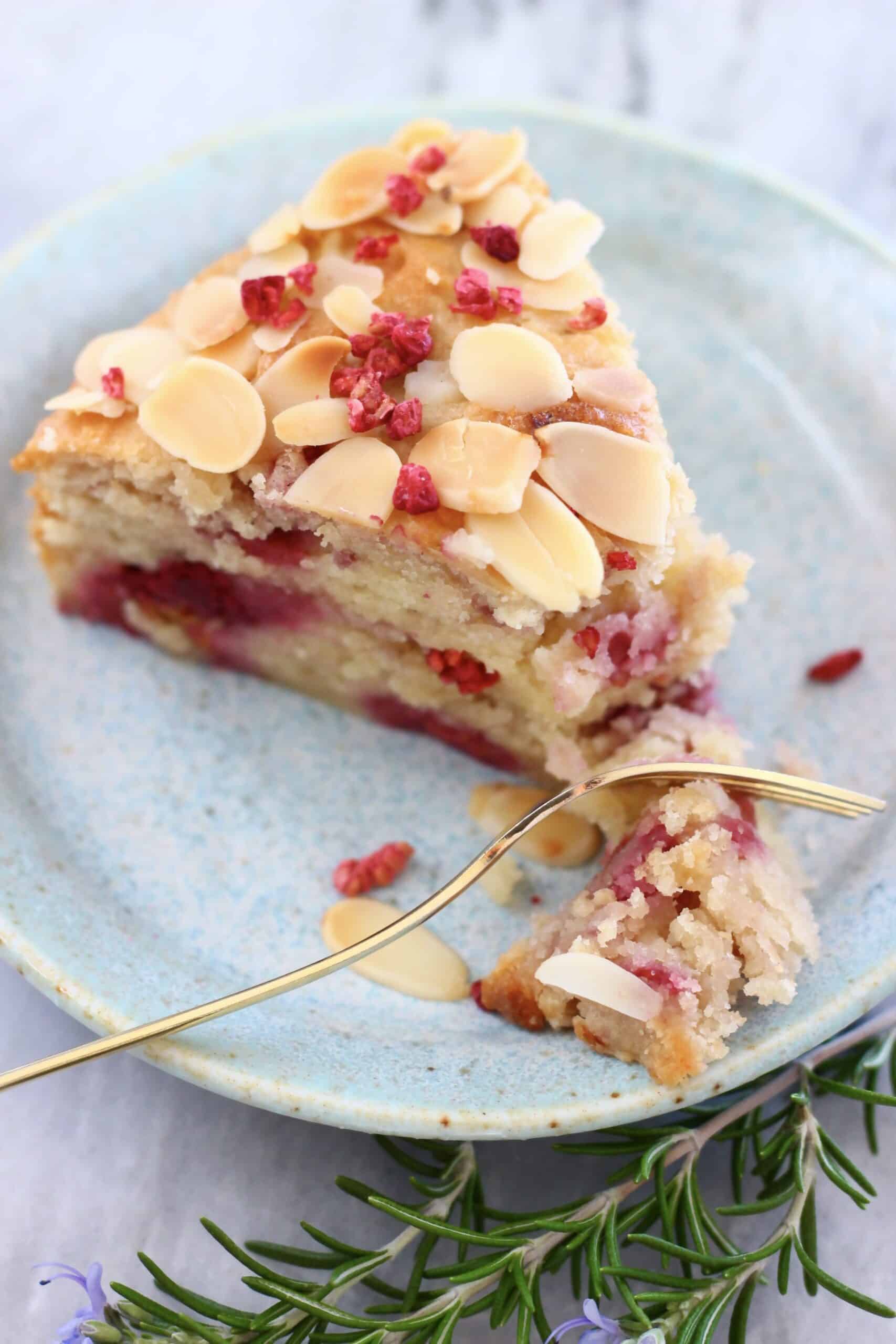 A slice of gluten-free vegan raspberry cake on a plate with a gold fork taking a bite