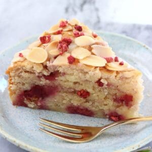 A slice of gluten-free vegan raspberry cake on a plate with a gold fork