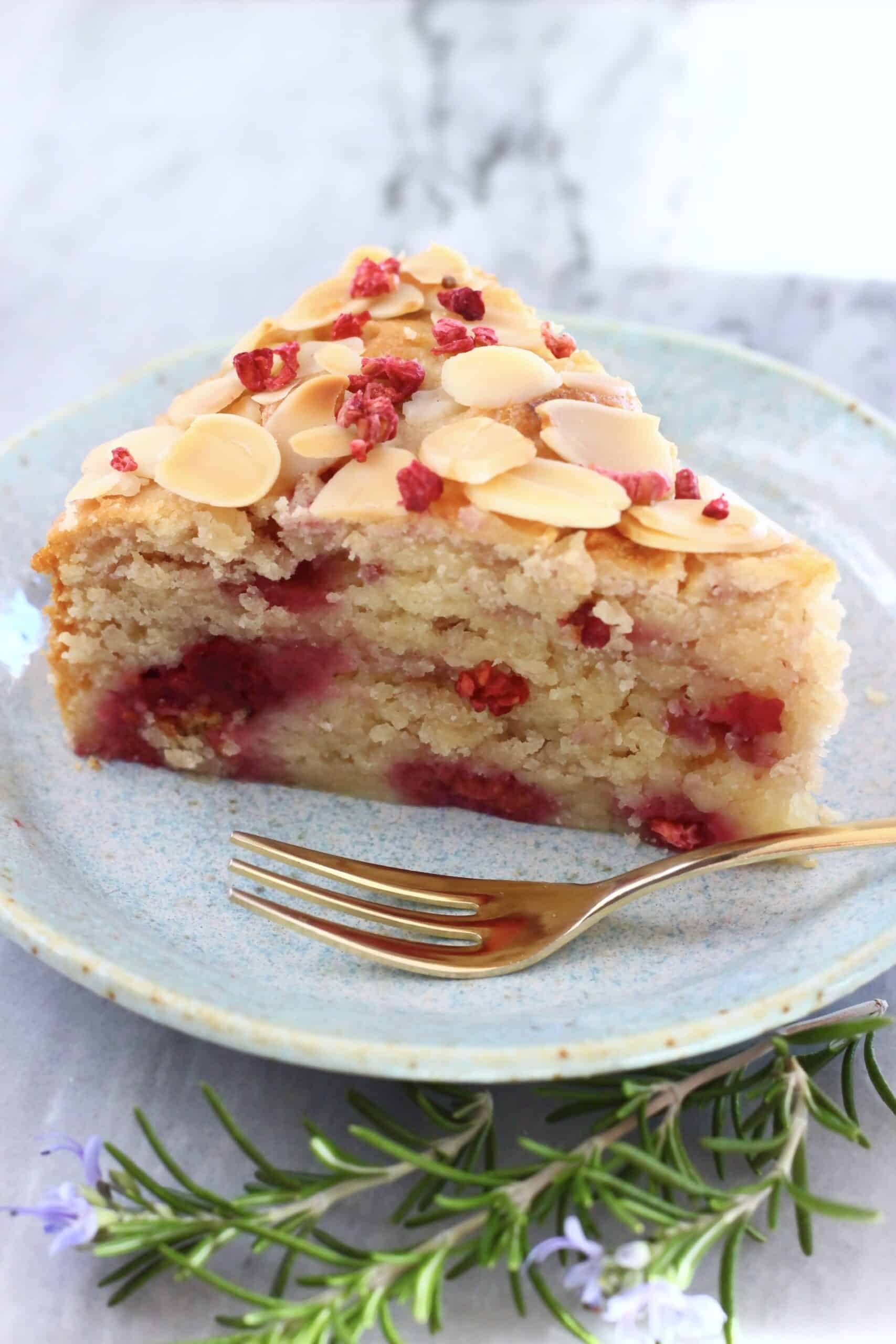 A slice of gluten-free vegan raspberry cake on a plate with a gold fork