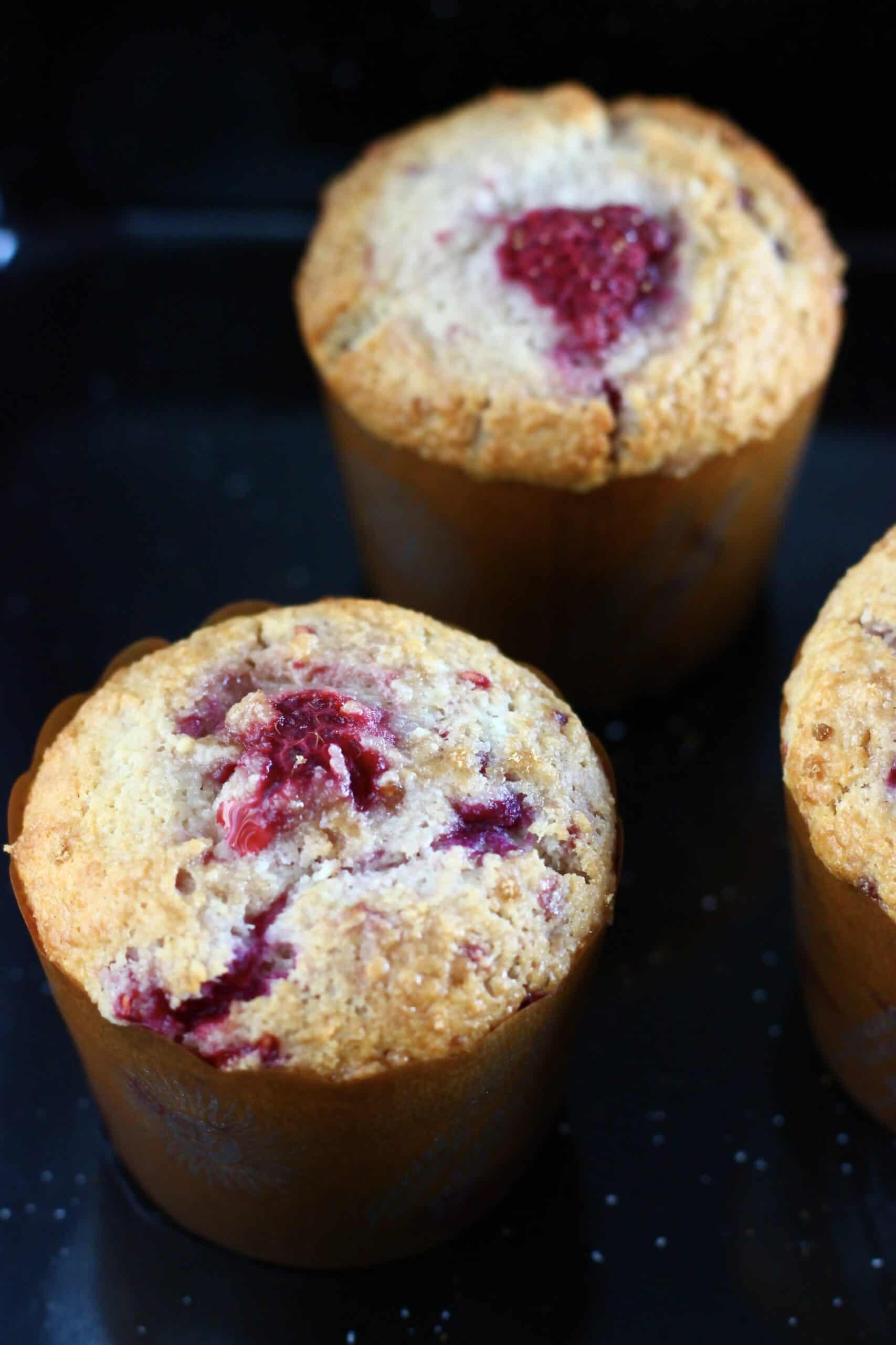 Three baked gluten-free vegan raspberry muffins in muffin cases