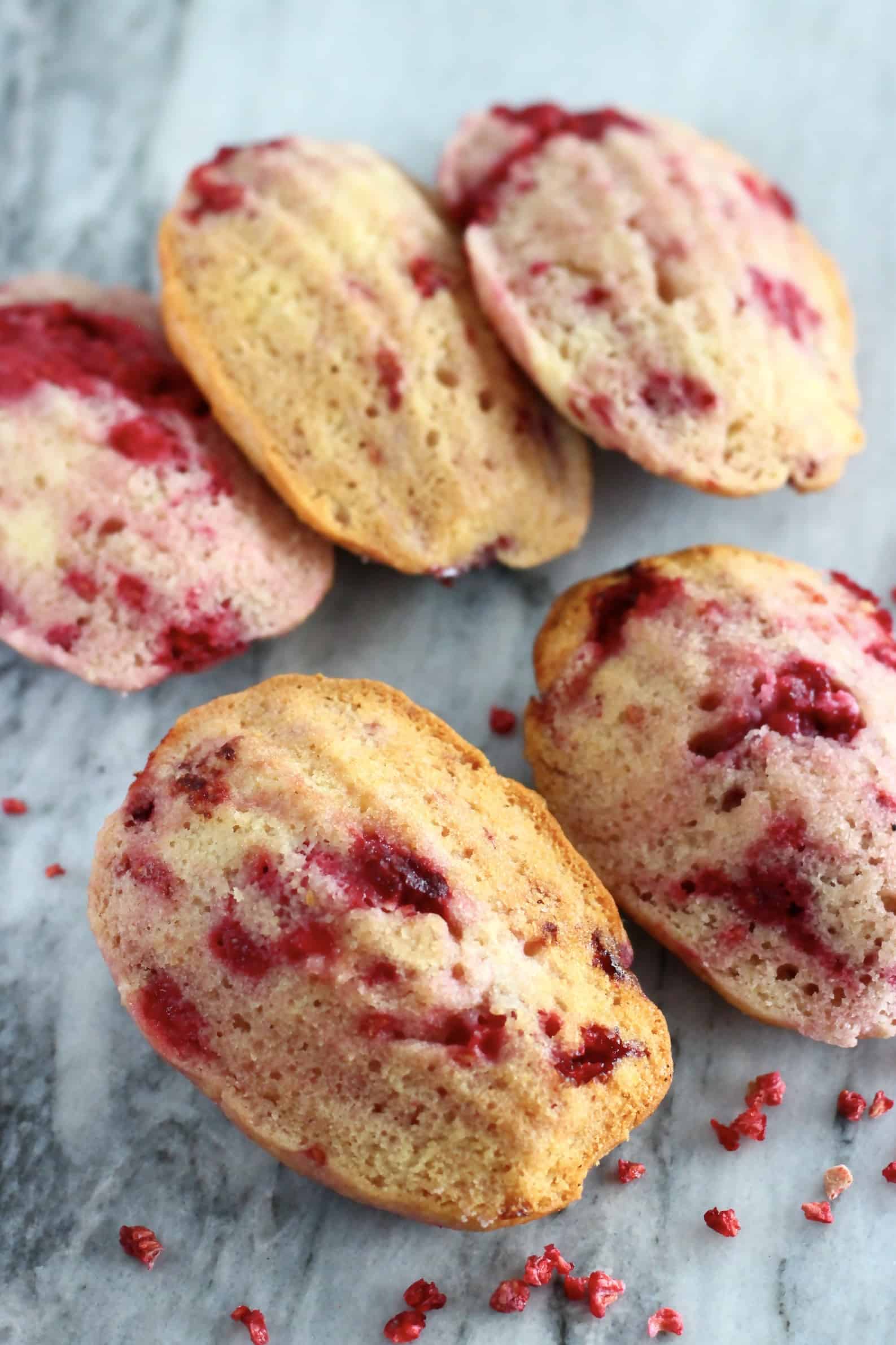 Five gluten-free vegan raspberry madeleines on a marble background