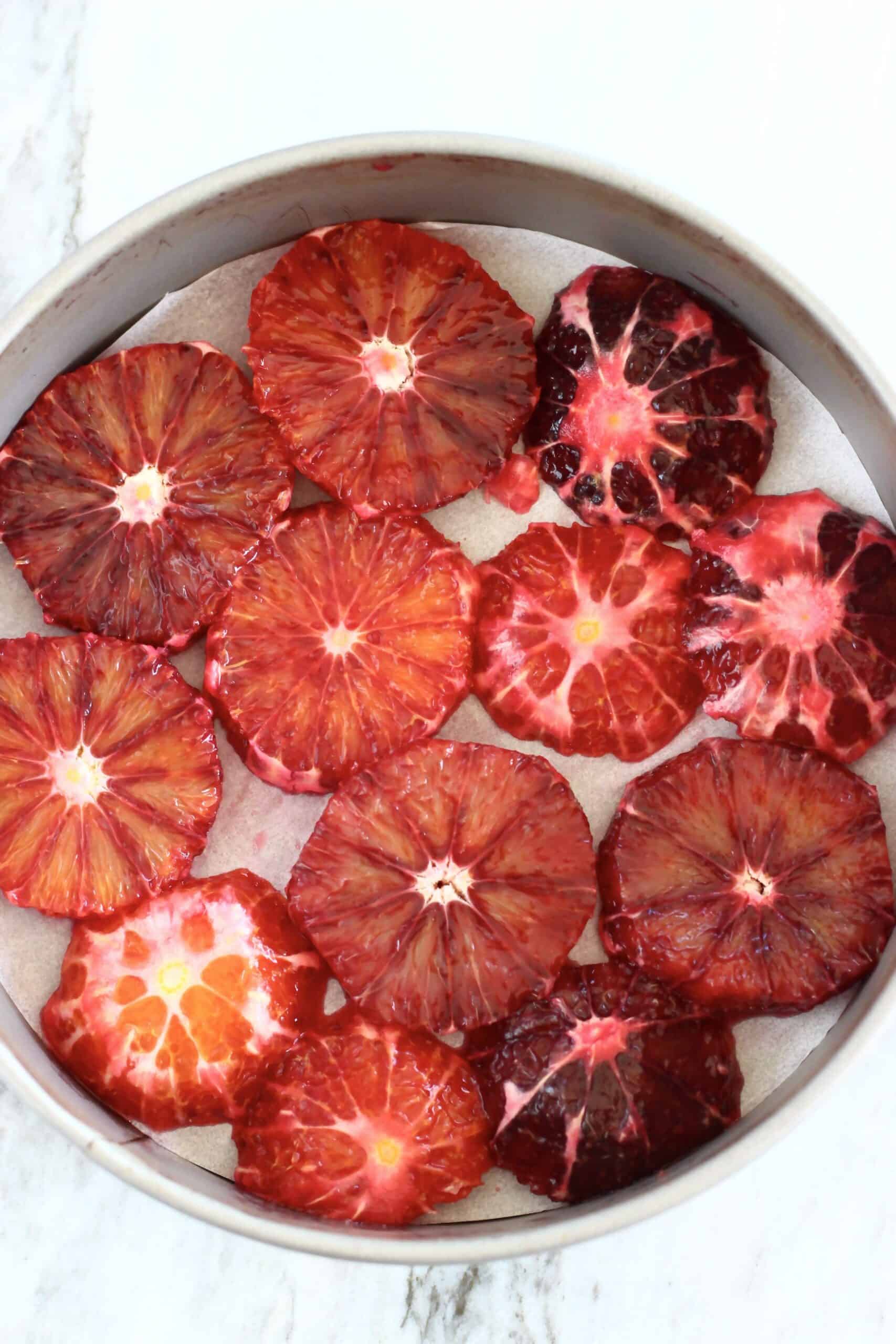 Blood orange slices laid out on the bottom of a round springform baking tin lined with baking paper