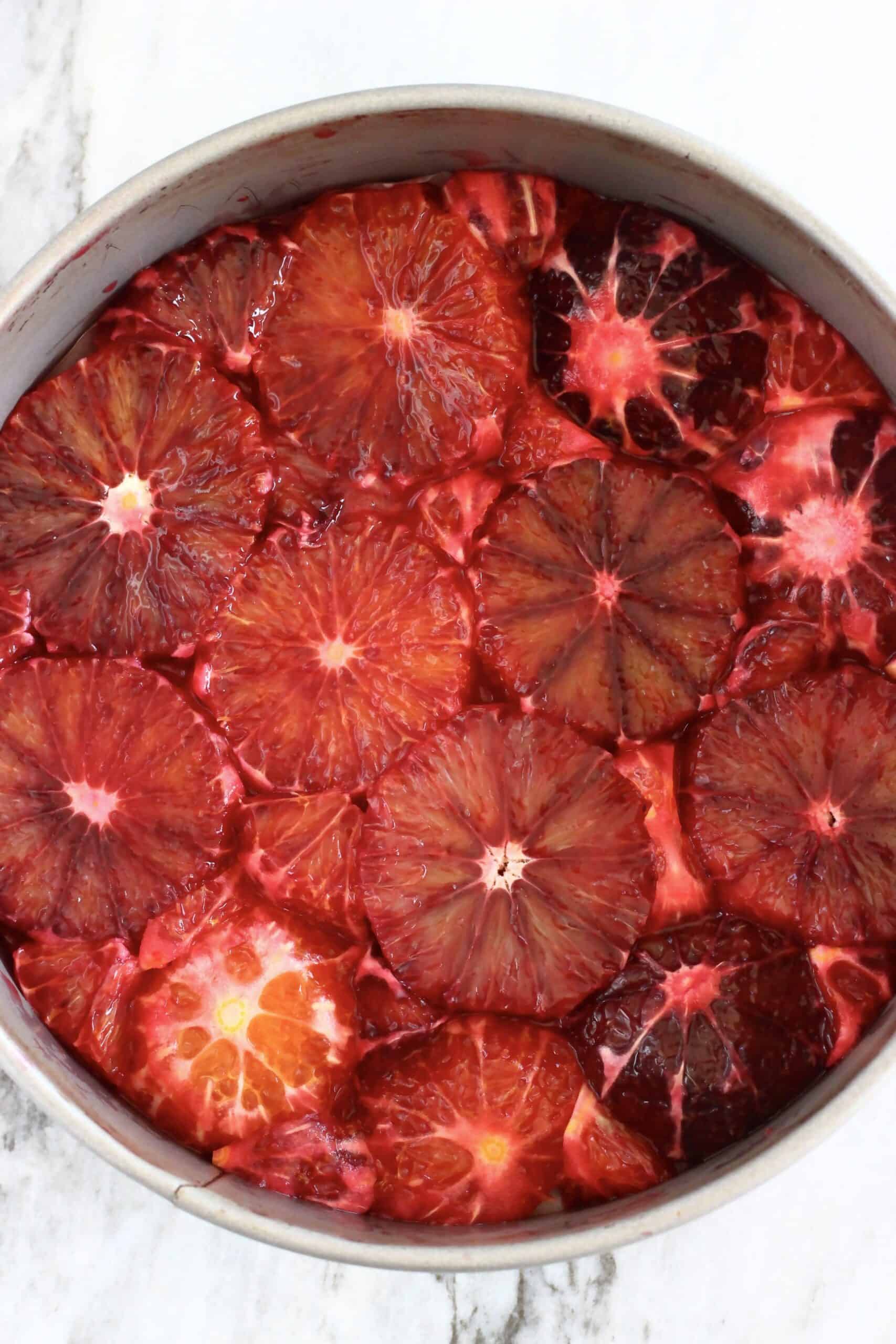 Blood orange slices laid out across the bottom of a round springform baking tin lined with baking paper