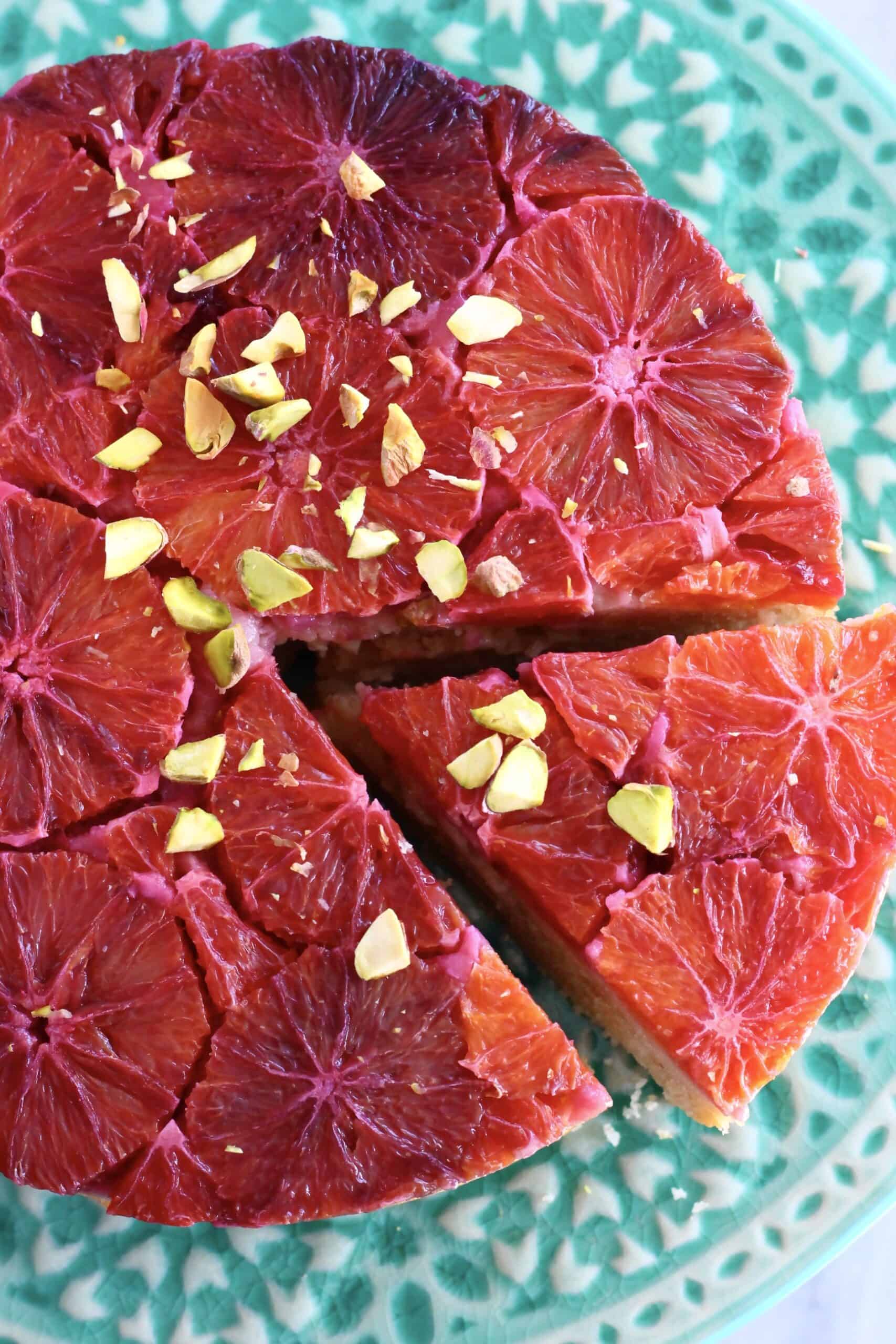 A gluten-free vegan blood orange cake on a cake stand with a slice taken out of it