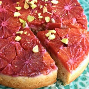 A gluten-free vegan blood orange cake on a cake stand with a slice taken out of it