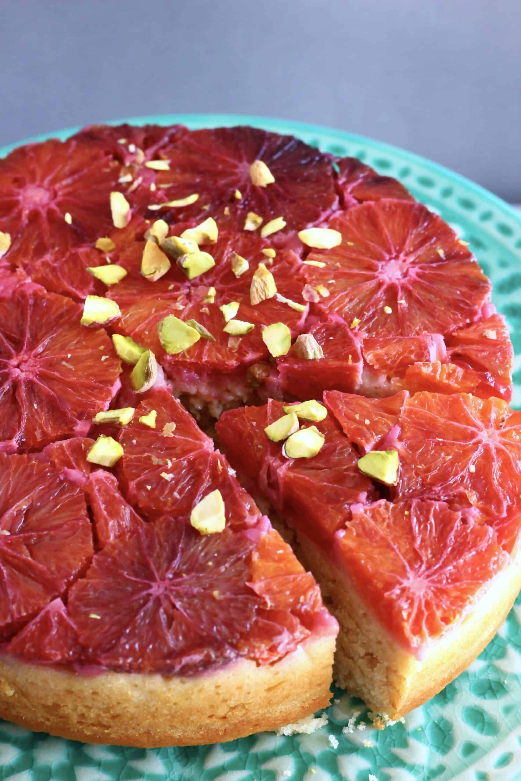 A gluten-free vegan blood orange cake on a cake stand with a slice taken out of it