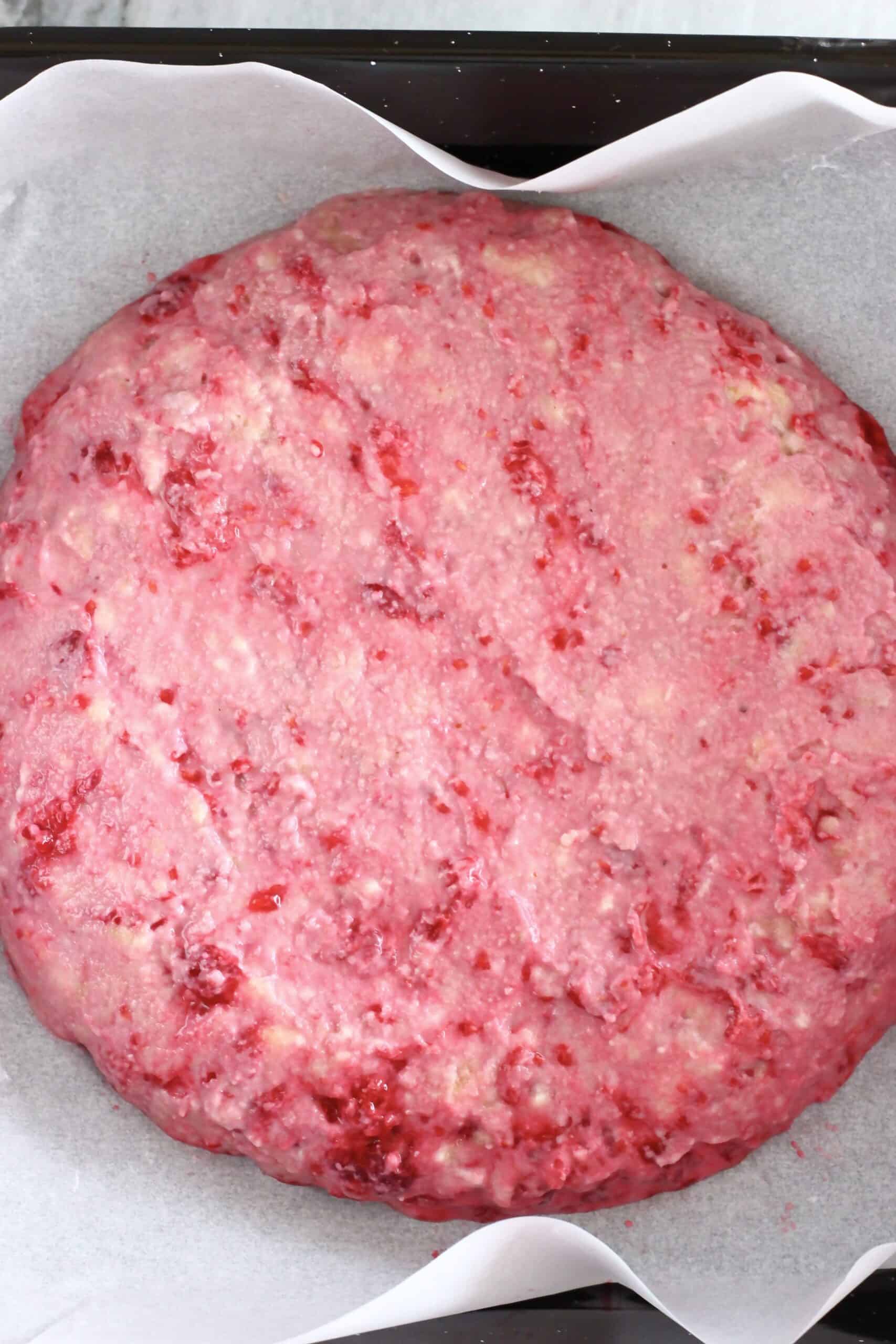 Raw gluten-free vegan raspberry scones batter in a round circle on a baking tray lined with baking paper