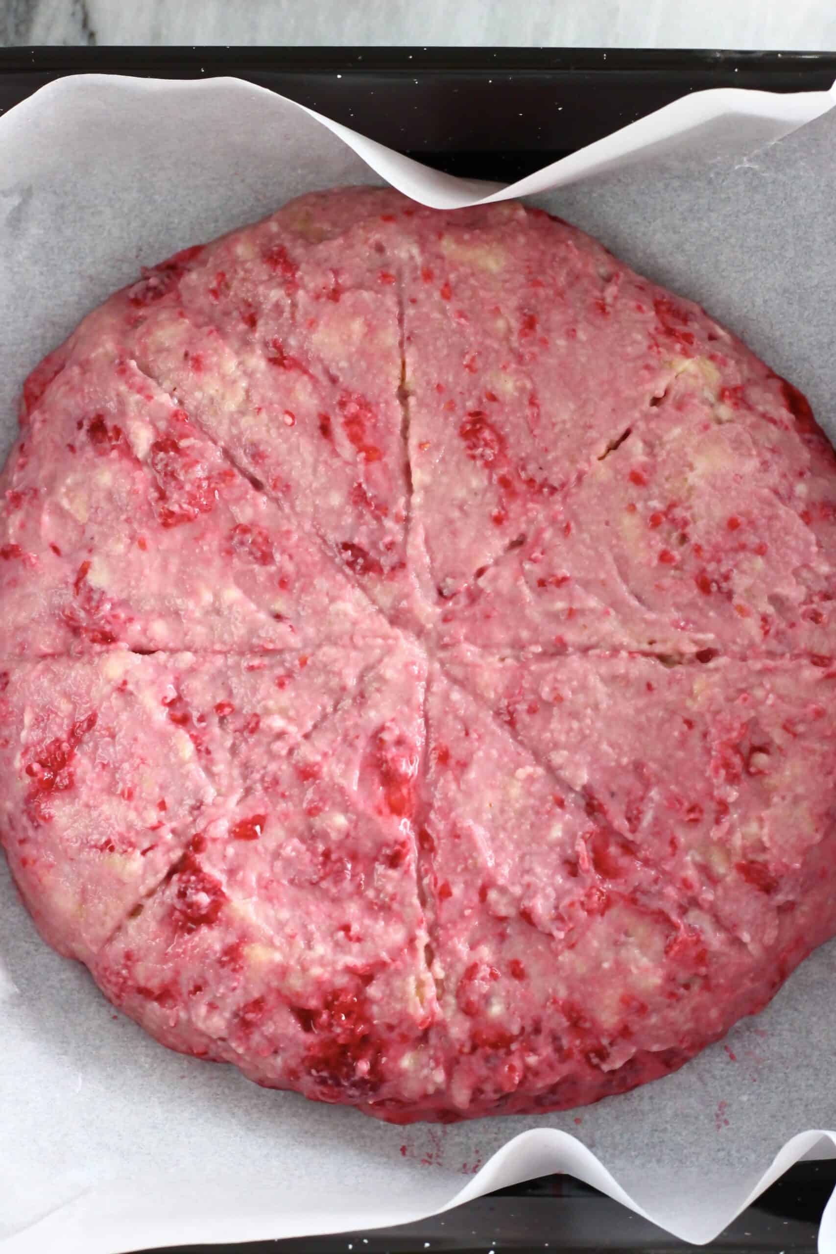 Raw gluten-free vegan raspberry scones batter in a round circle scored into 8 pieces on a baking tray lined with baking paper