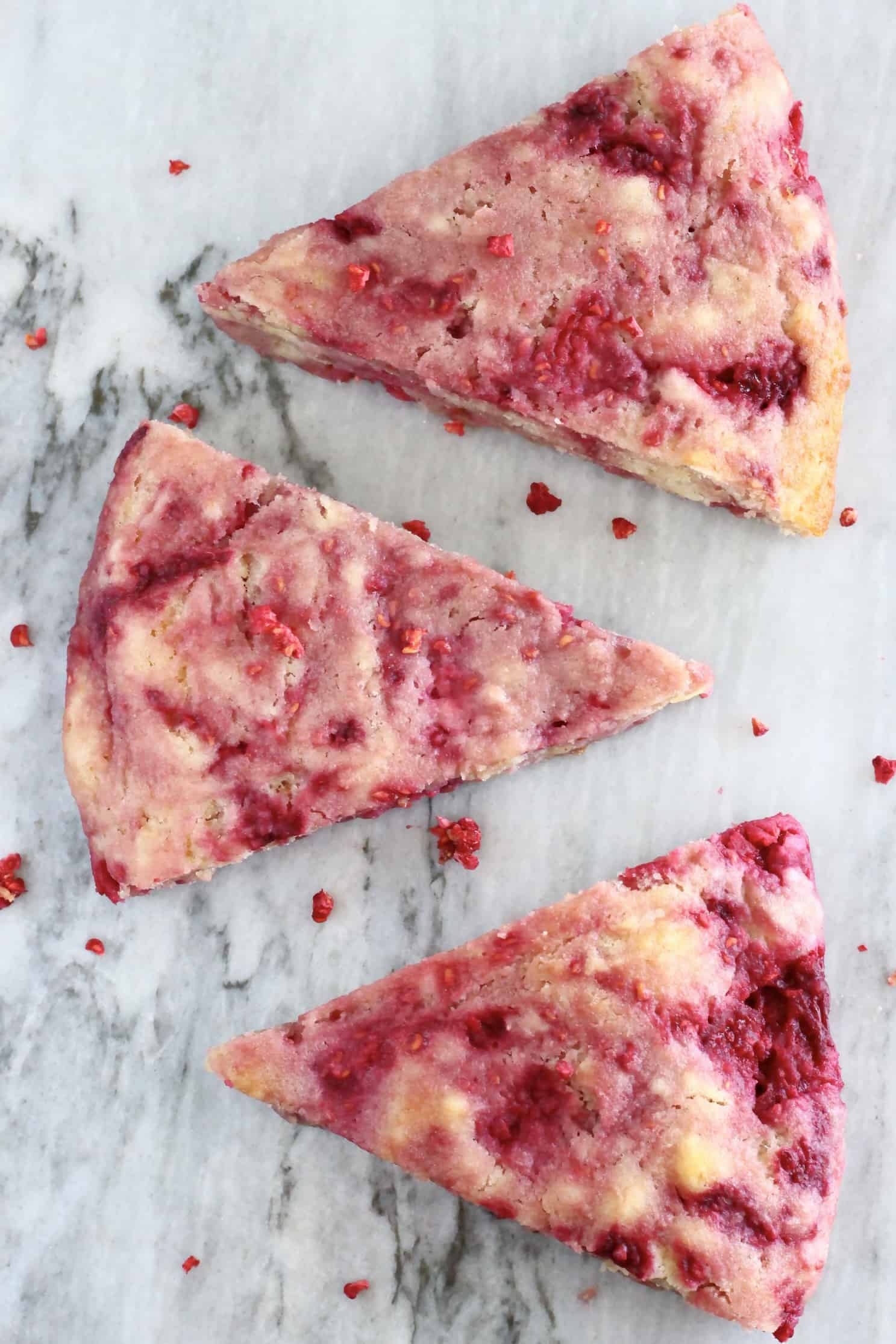 Three triangular gluten-free vegan raspberry scones on a marble background