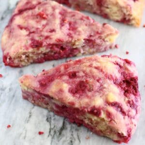 Three triangular gluten-free vegan raspberry scones on a marble background