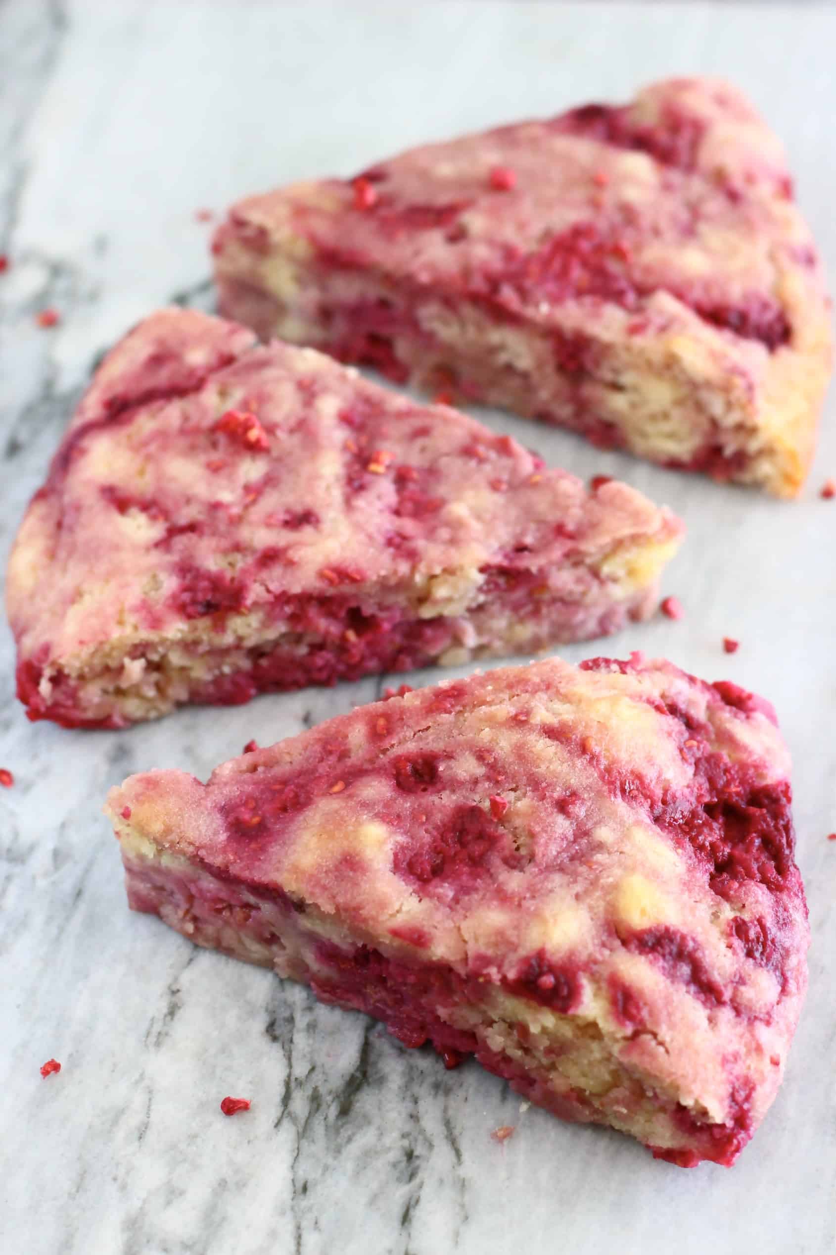 Three triangular gluten-free vegan raspberry scones on a marble background