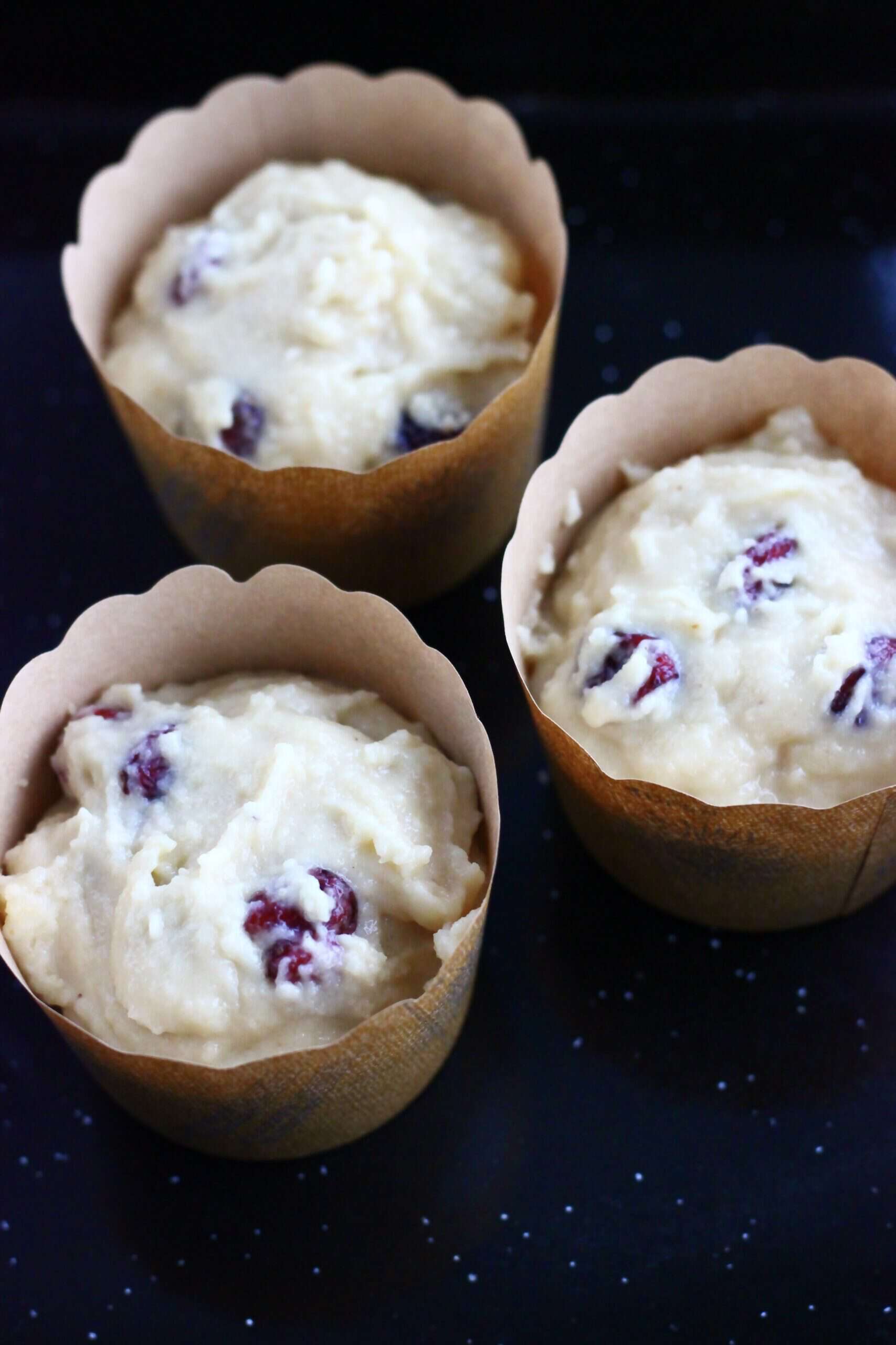 Raw gluten-free vegan cranberry muffins batter in muffin cases in a muffin tin