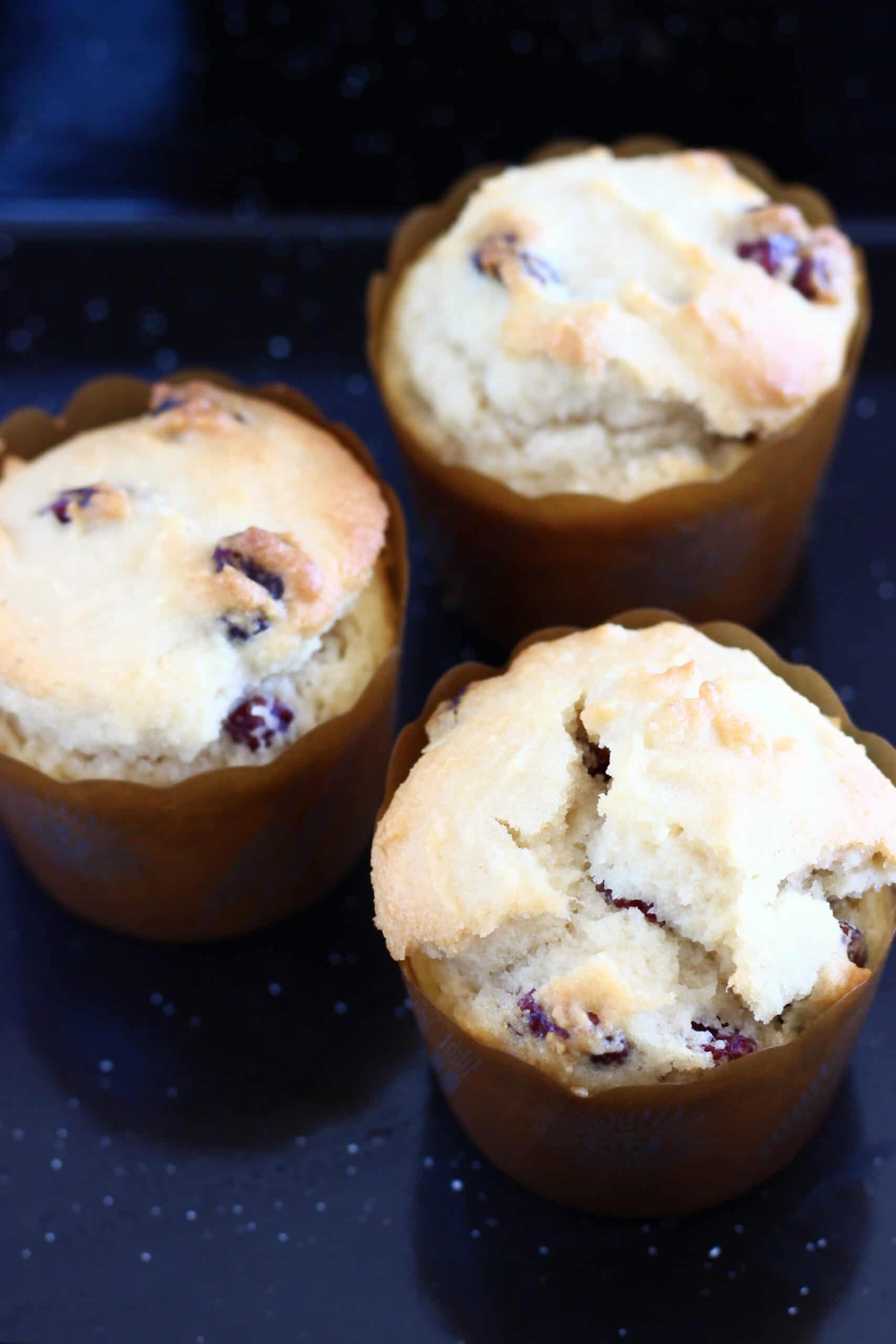 Three gluten-free vegan cranberry muffins in muffin cases in a muffin tin
