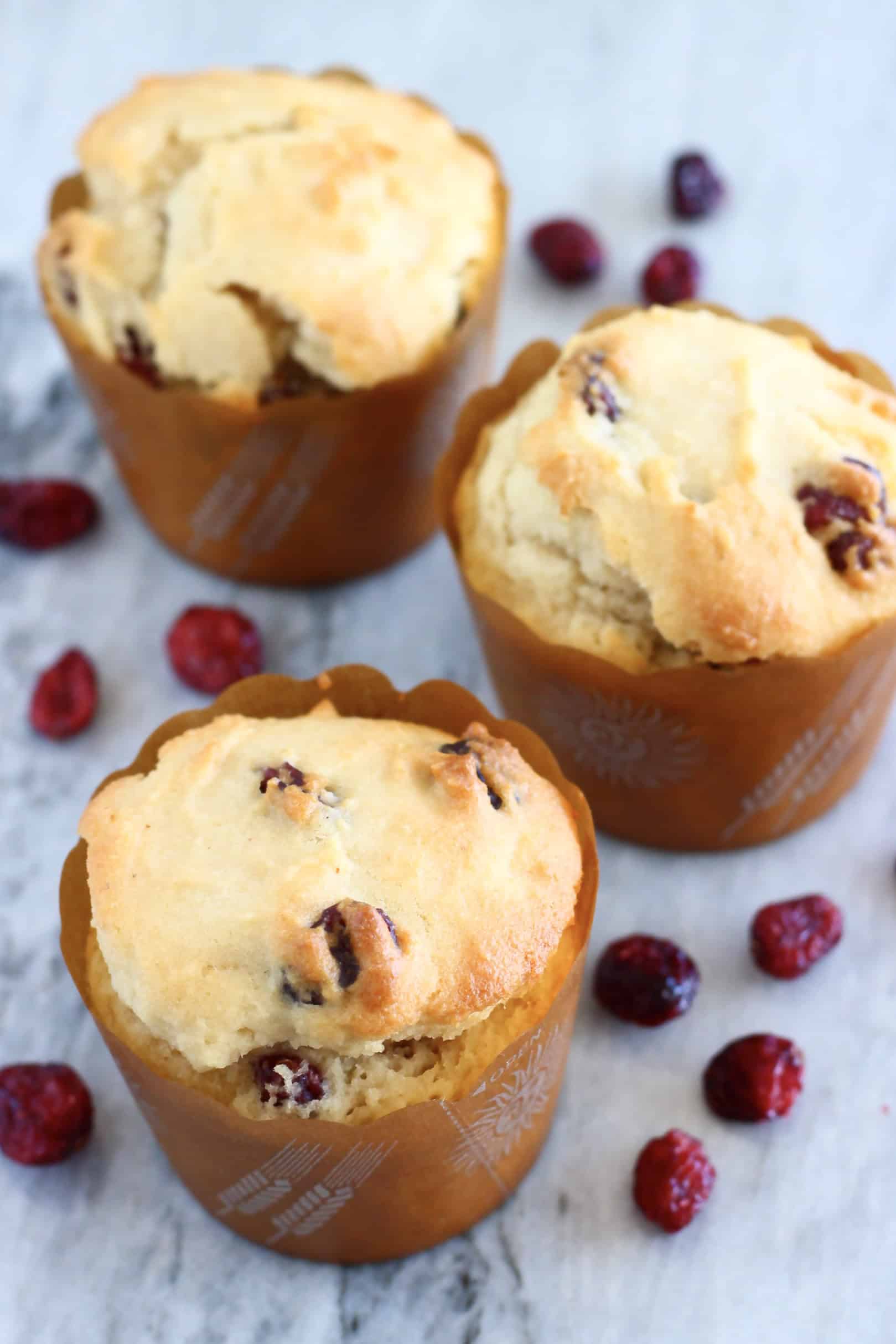 Three baked gluten-free vegan cranberry muffins on a marble background