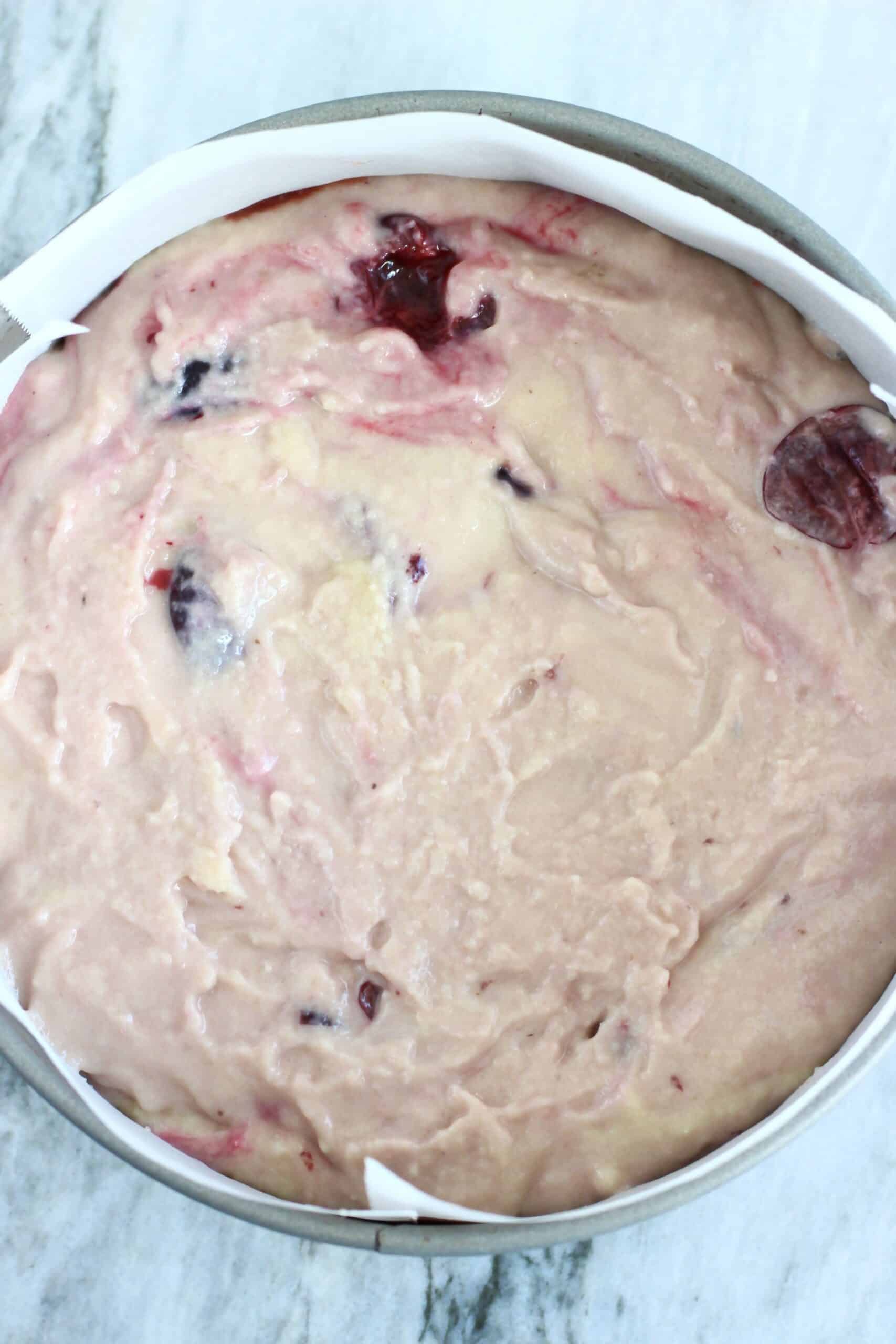 Raw gluten-free vegan cherry cake batter in a round springform baking tin lined with baking paper