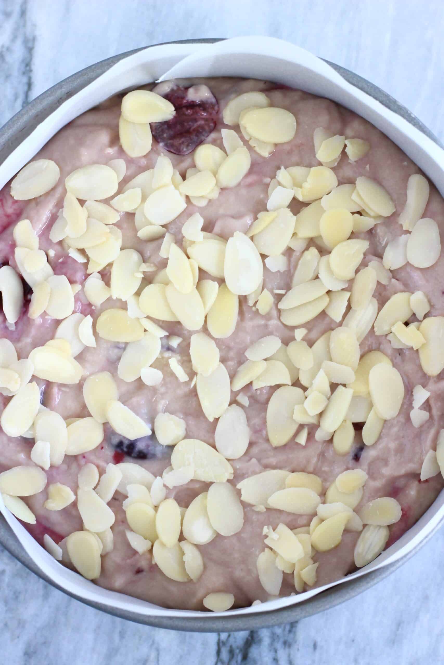 Raw gluten-free vegan cherry cake batter in a round springform baking tin lined with baking paper topped with flaked almonds