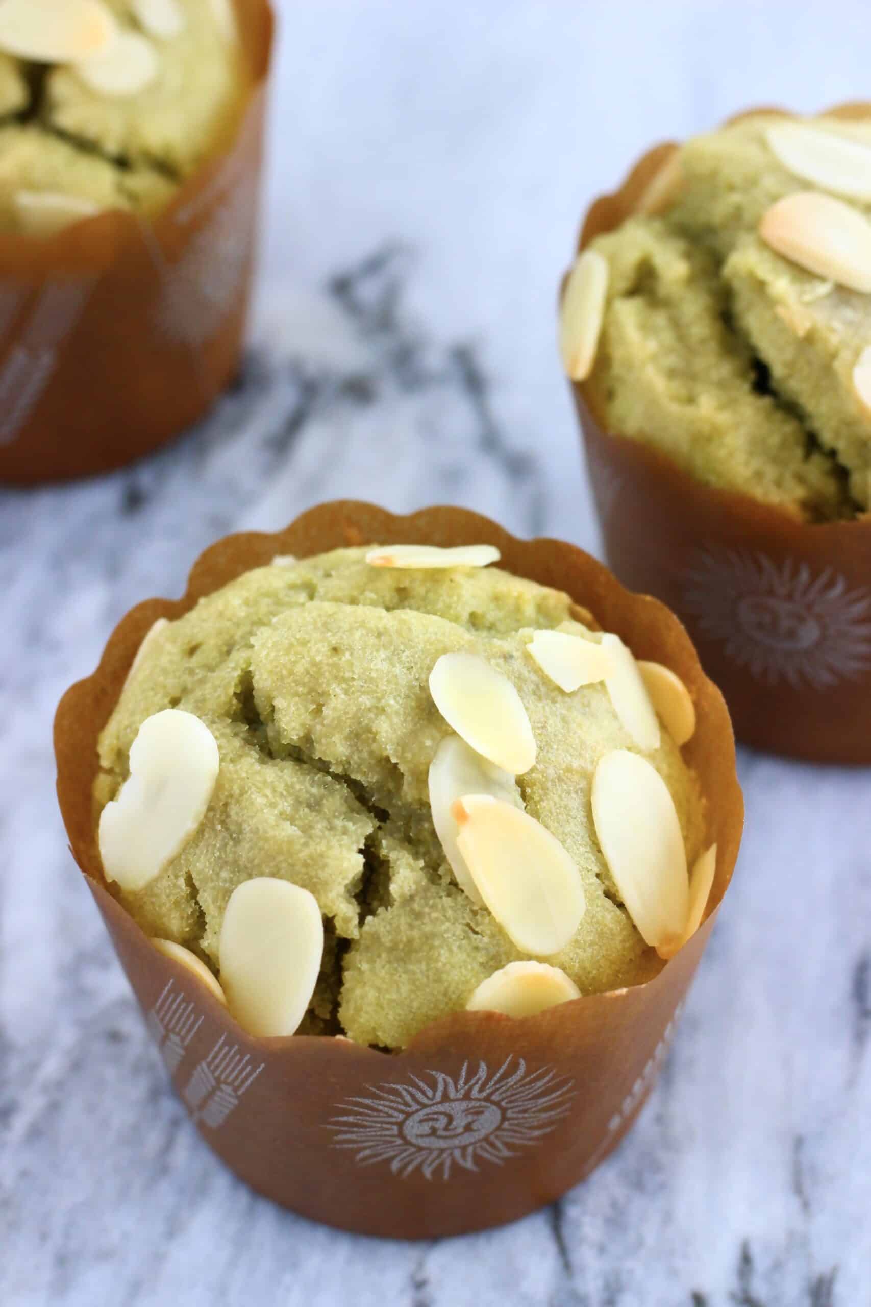 Three gluten-free vegan matcha muffins in muffin cases on a marble background