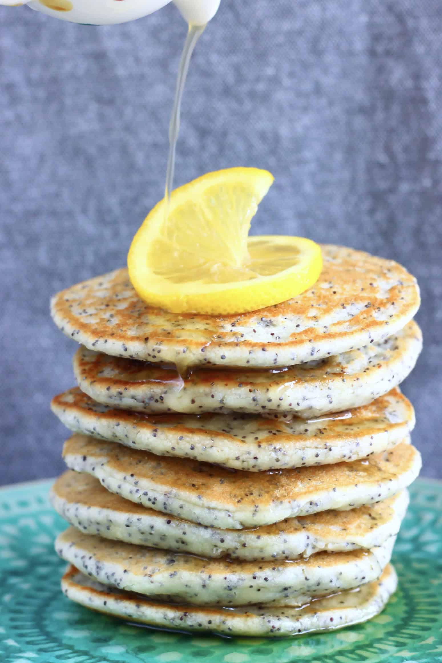 A stack of gluten-free vegan lemon poppy seed pancakes on a plate with syrup being poured over