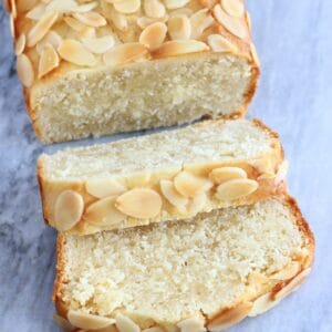 A gluten-free vegan almond loaf cake with two slices cut from it on a marble background