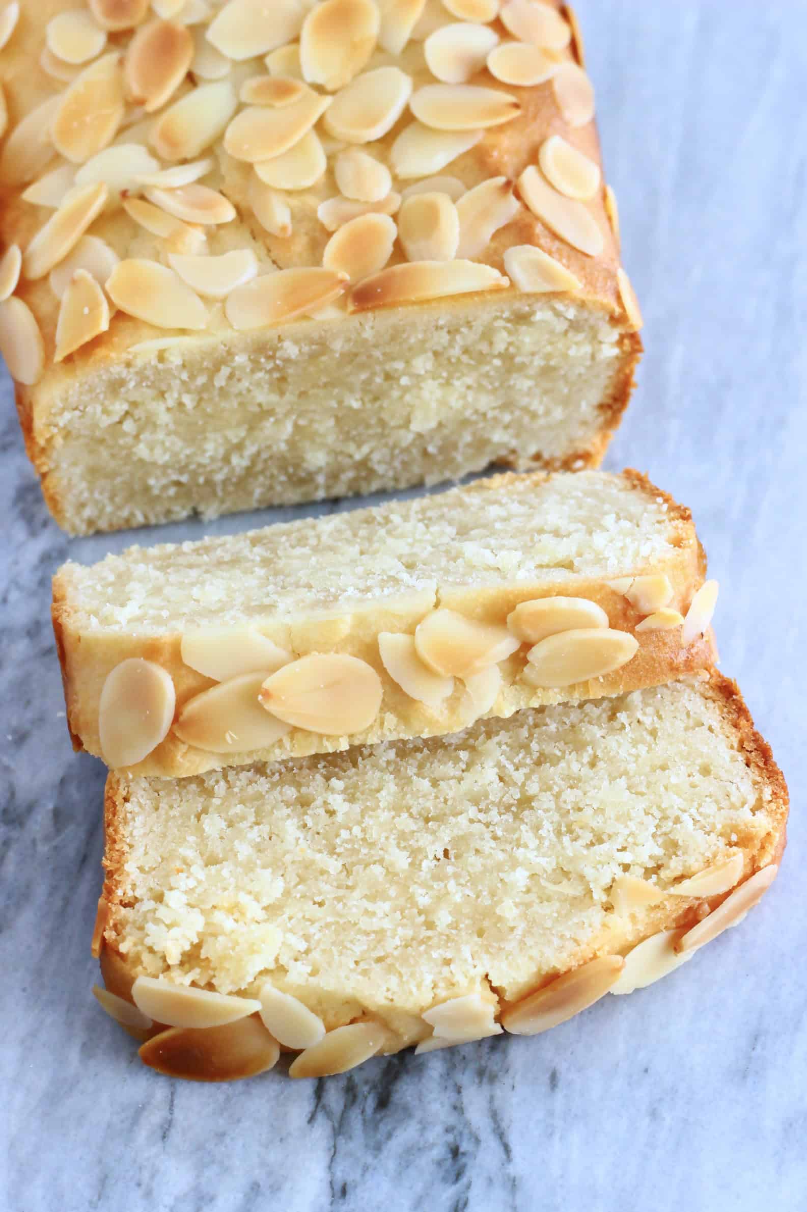 A gluten-free vegan almond loaf cake with two slices cut from it on a marble background